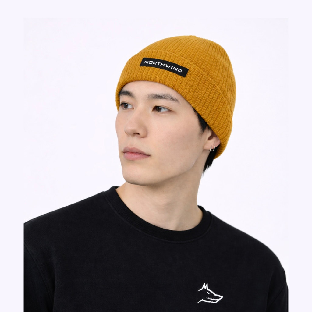 Person wearing a mustard yellow organic cotton beanie with 'Northwind' branding on a white background