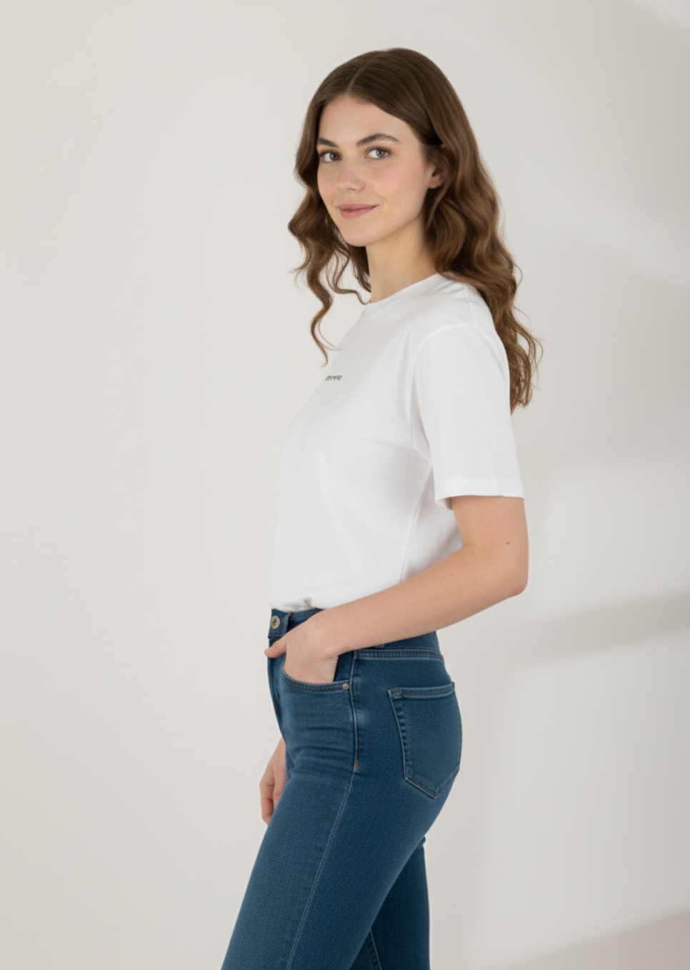 Woman wearing an Essential White T-shirt with Wolf Logo Embroidery and blue jeans against a plain background