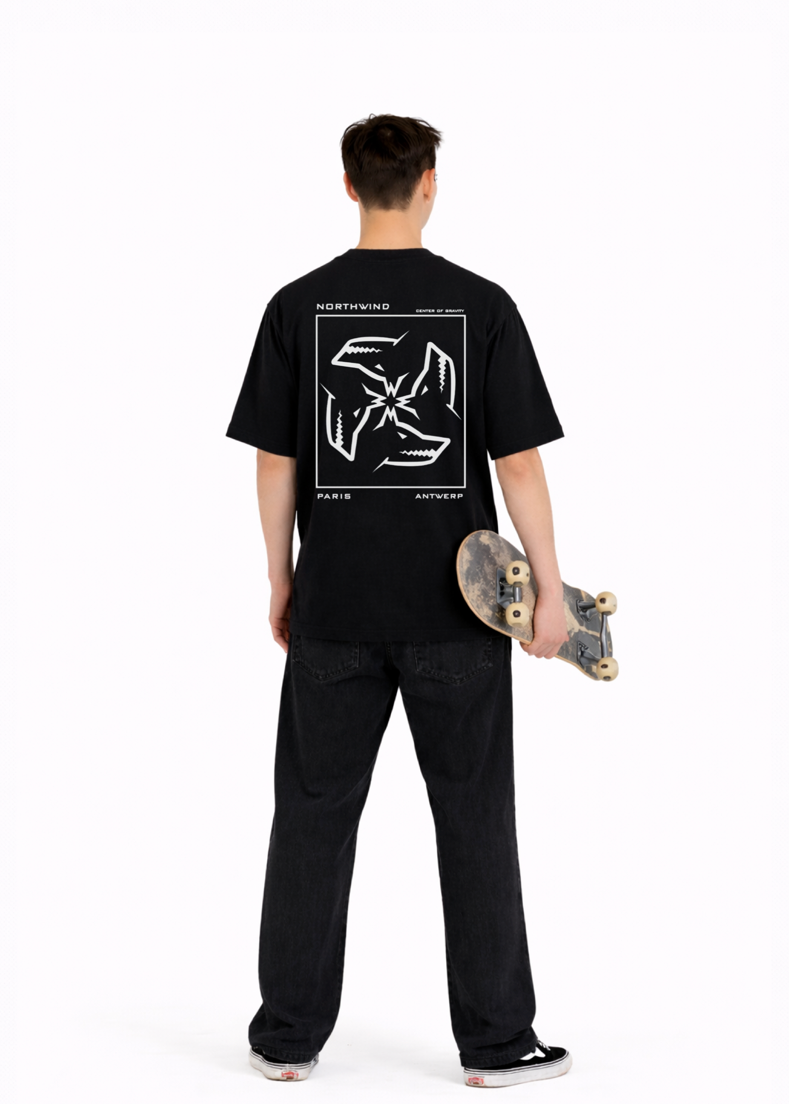 Young adult wearing a Northwind oversized organic cotton black t-shirt with Northwind embroidered on the chest, center of gravity design screen printed on the back, Carhartt pants, black Vans shoes, skating