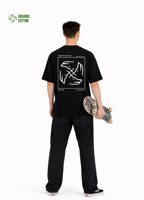 Young adult wearing a Northwind oversized organic cotton black t-shirt with Northwind embroidered on the chest, center of gravity design screen printed on the back, Carhartt pants, black Vans shoes, skating