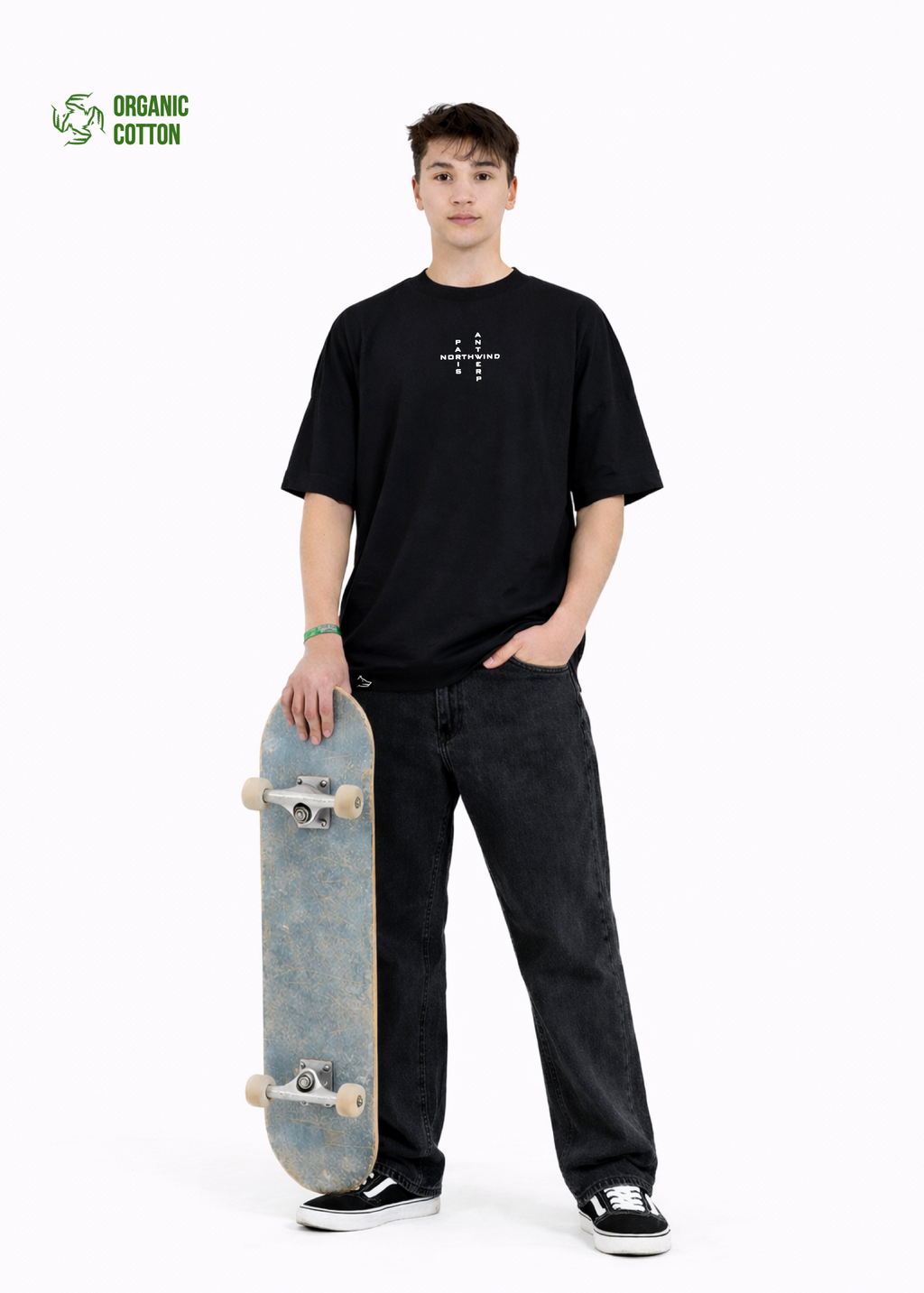 Young adult wearing a Northwind oversized organic cotton black t-shirt with Northwind crossword ANTWERP and PARIS logo embroidered on the chest, Carhartt pants, black Vans shoes, holding a skate board