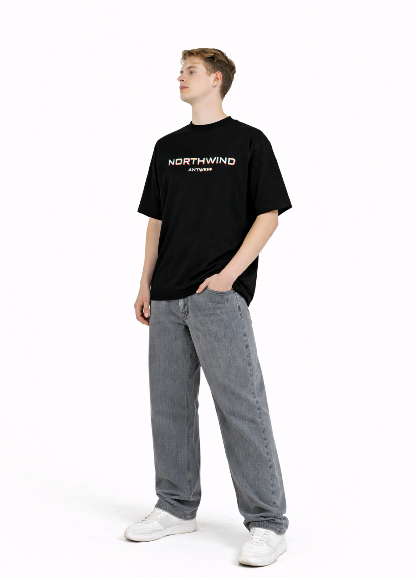 Person wearing a black organic cotton oversized 'Northwind' t-shirt and gray pants on a white background
