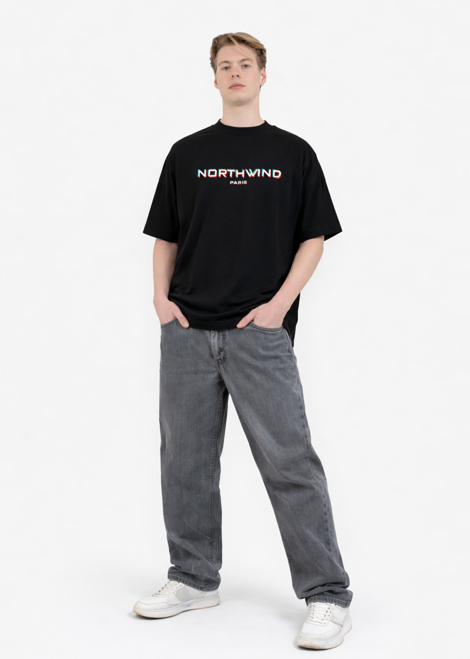 Person wearing a black organic cotton oversized 'Northwind' t-shirt with glitch design on the chest and gray pants on a white background