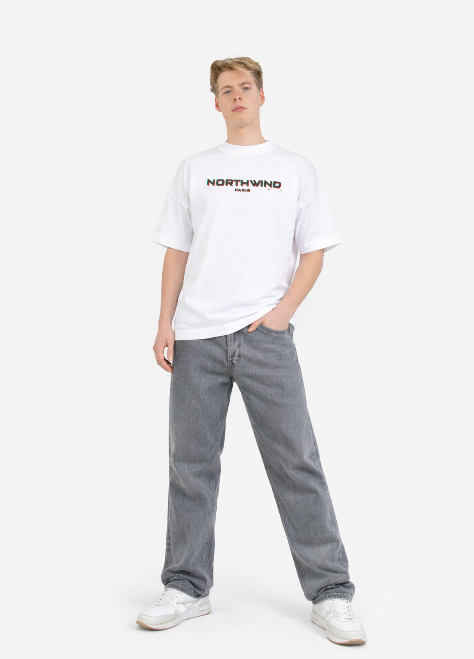 Person wearing a white organic cotton oversized 'Northwind' t-shirt with glitch design on the chest and gray pants on a white background