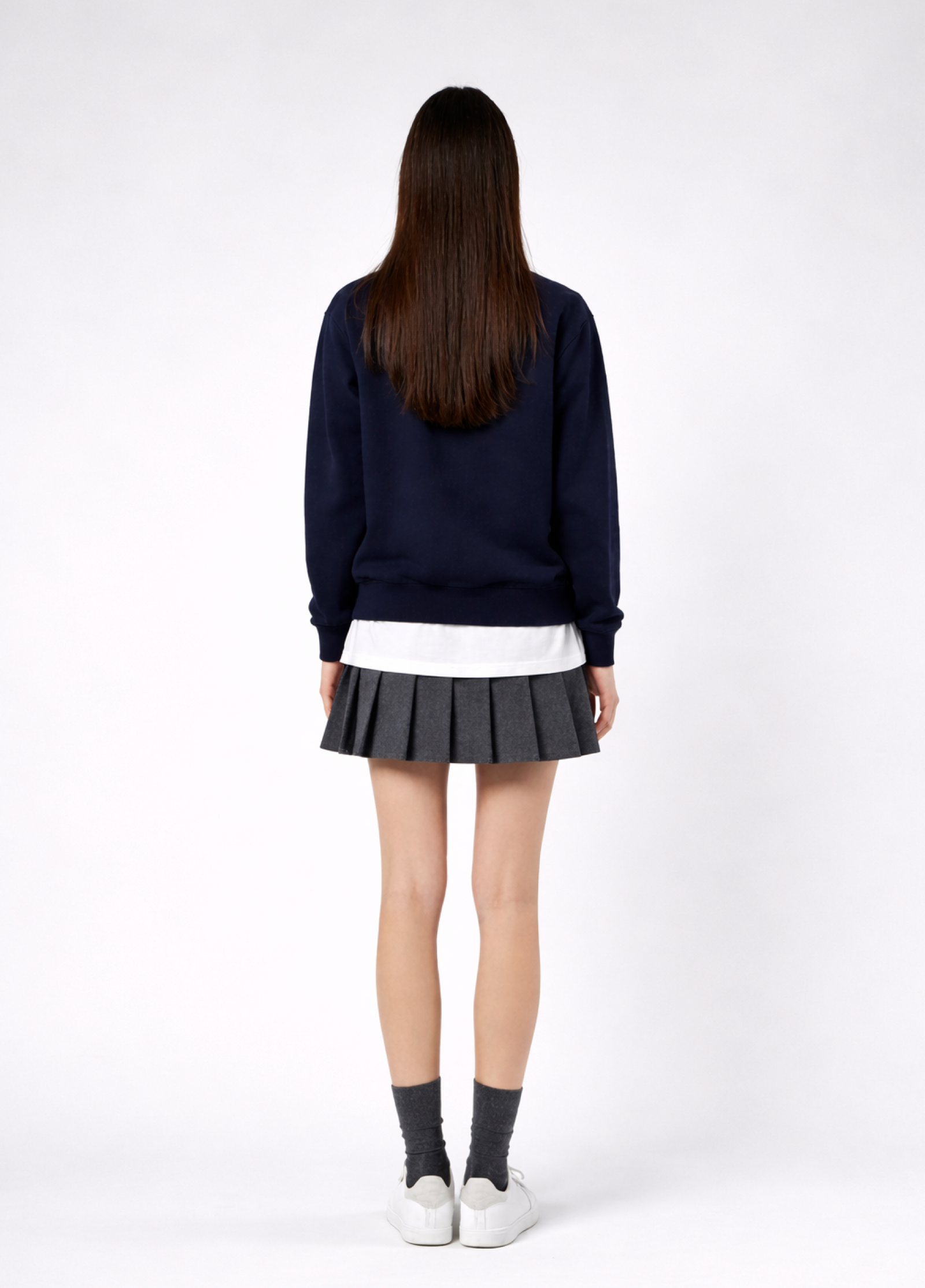a woman wearing a french navy Northwind Lone wolf sweatshirt, white Northwind t-shirt under, pleated skirt, and white shoes on a white background