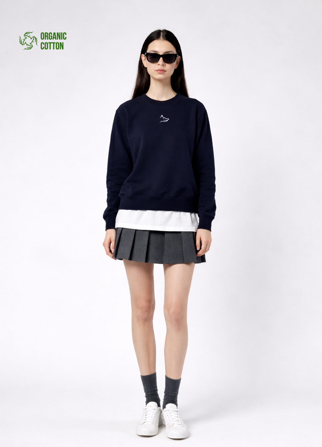 a woman wearing a french navy Northwind Lone wolf sweatshirt with Northwind embroidered wolf logo on the chest, white Northwind t-shirt under, pleated skirt, and white shoes on a white background
