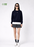 a woman wearing a french navy Northwind Lone wolf sweatshirt with Northwind embroidered wolf logo on the chest, white Northwind t-shirt under, pleated skirt, and white shoes on a white background