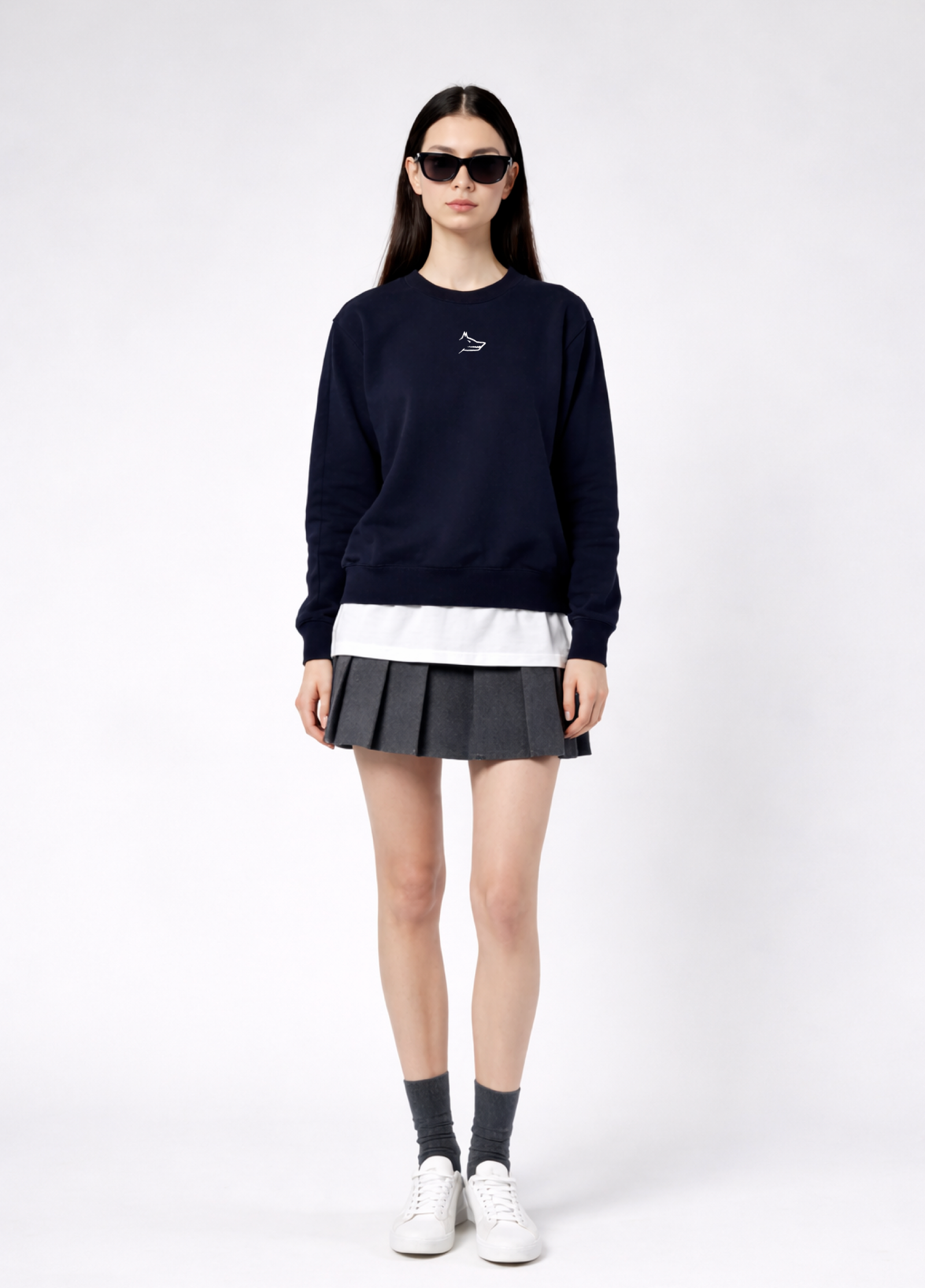 a woman wearing a french navy Northwind Lone wolf sweatshirt with Northwind embroidered wolf logo on the chest, white Northwind t-shirt under, pleated skirt, and white shoes on a white background