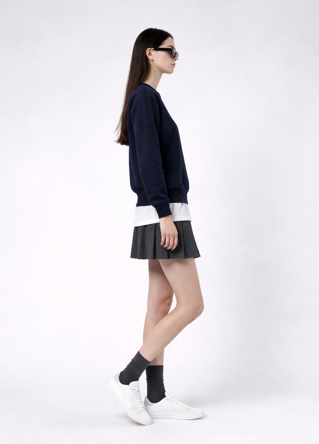 a woman wearing a french navy Northwind Lone wolf sweatshirt with Northwind embroidered wolf logo on the chest, white Northwind t-shirt under, pleated skirt, and white shoes on a white background