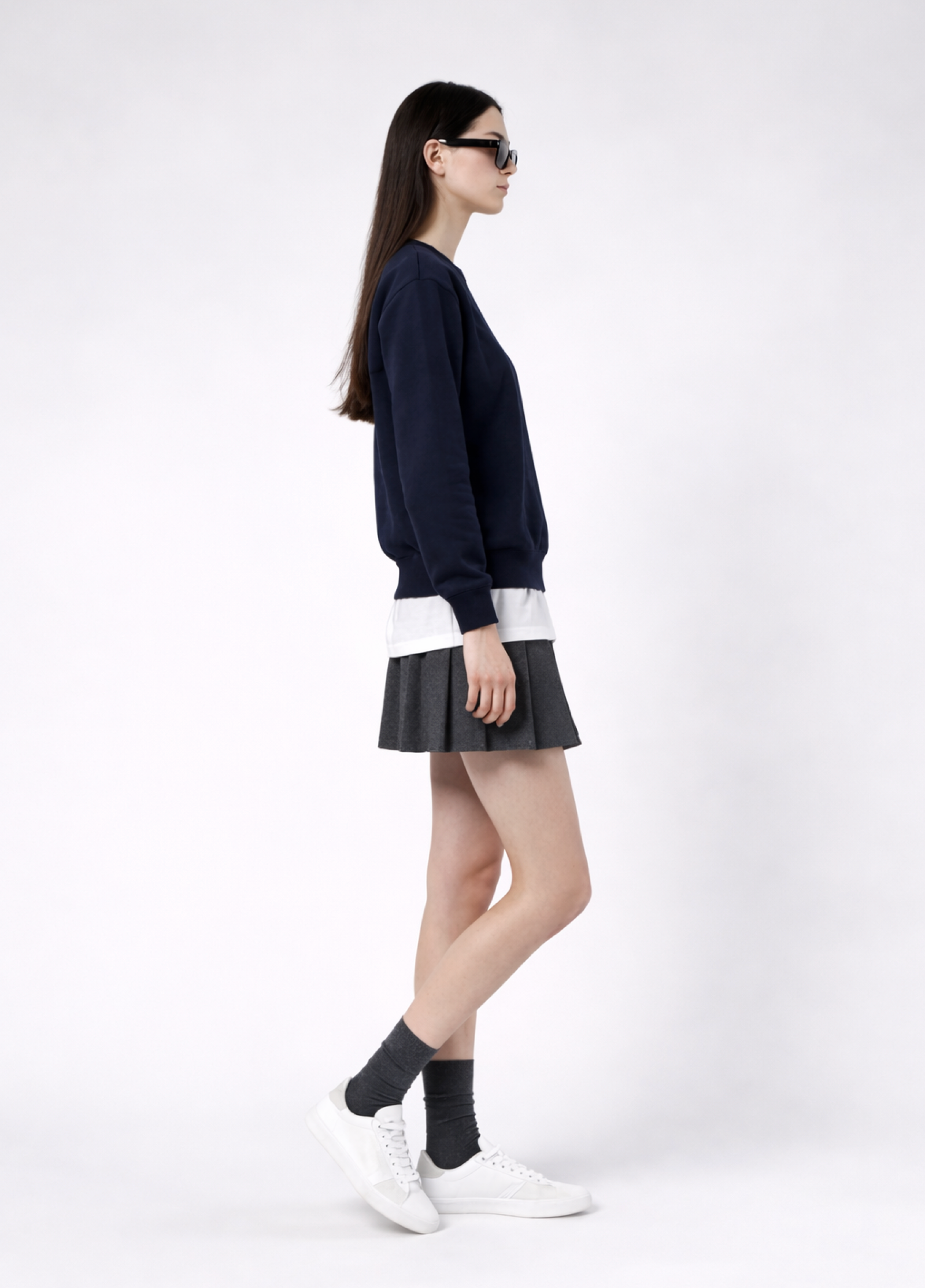 a woman wearing a french navy Northwind Lone wolf sweatshirt with Northwind embroidered wolf logo on the chest, white Northwind t-shirt under, pleated skirt, and white shoes on a white background