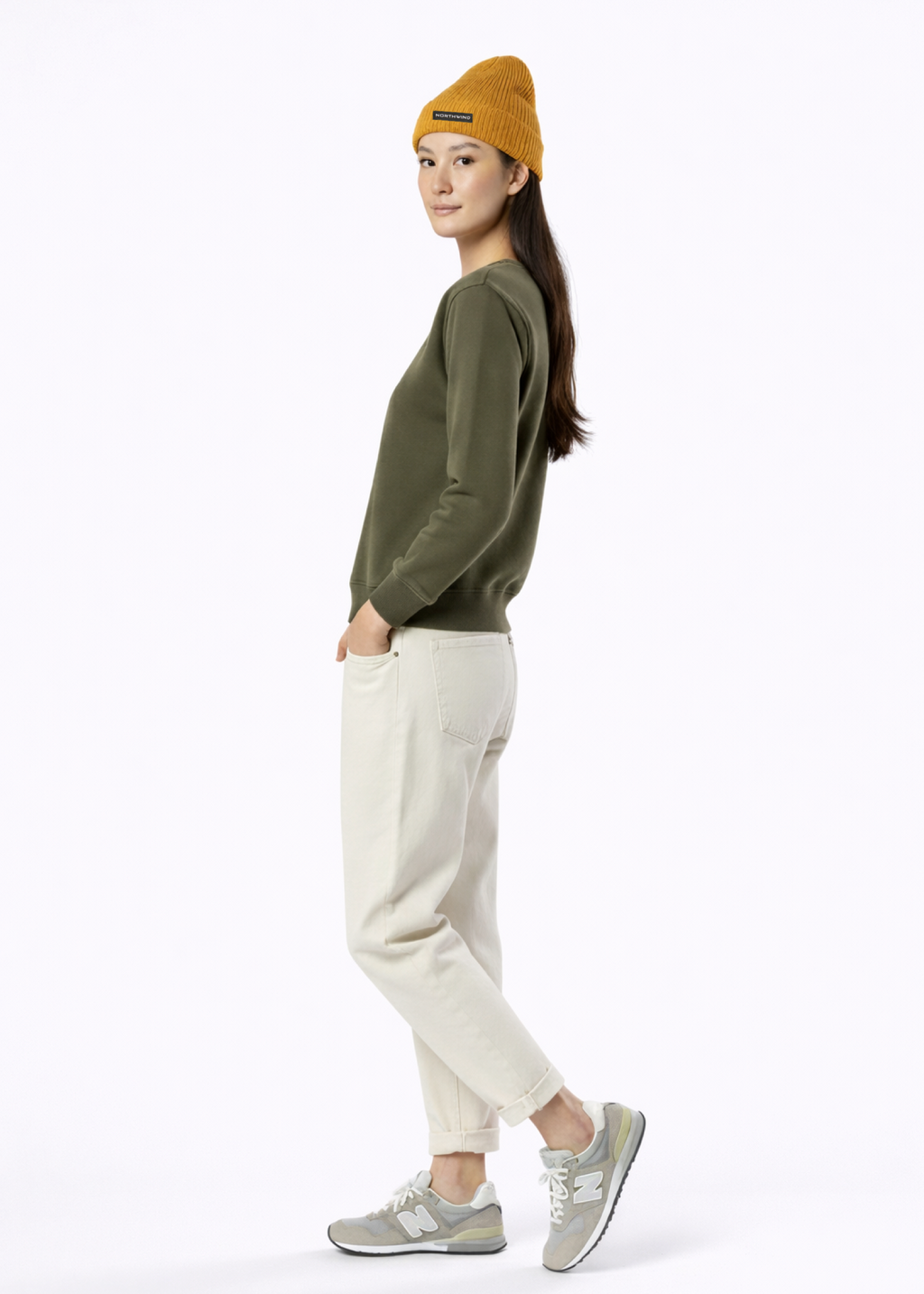 A woman wearing a khaki green Northwind Lone wolf sweatshirt with Northwind wolf embroidered logo on the chest, Northwind organic mustard beanie 