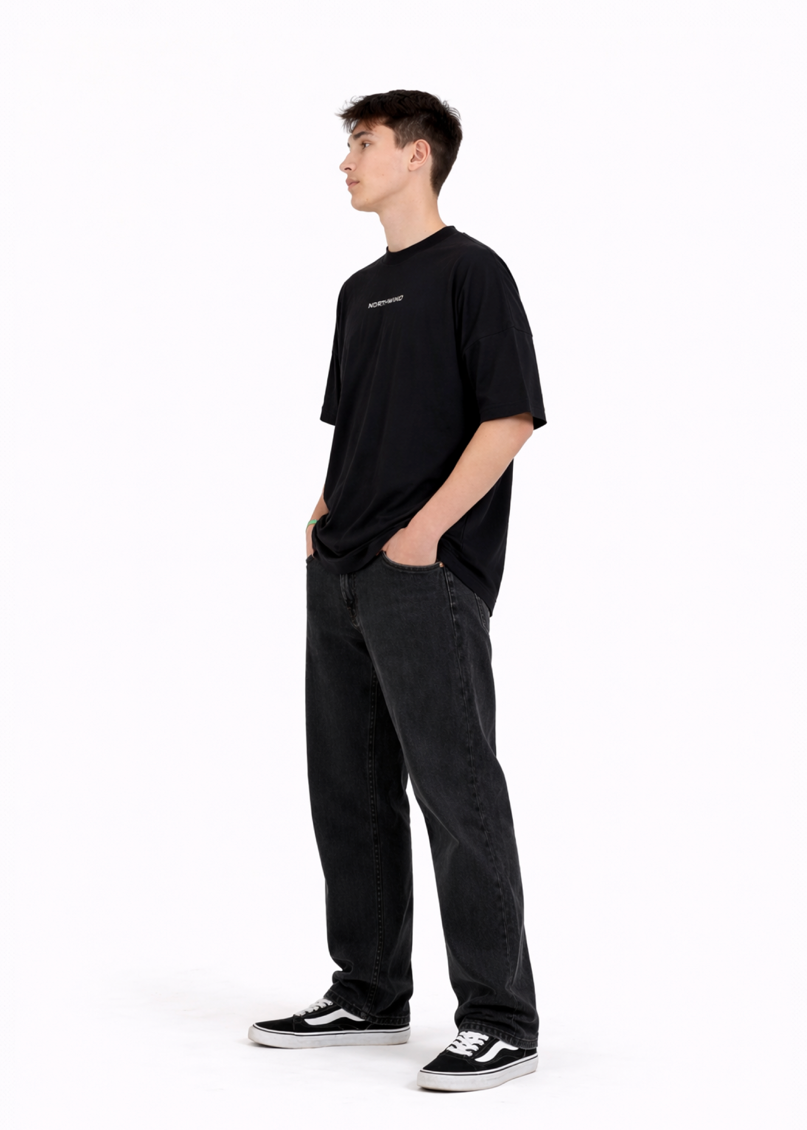 Young adult wearing a Northwind oversized organic cotton black t-shirt with Northwind embroidered on the chest, Carhartt pants, black Vans shoes