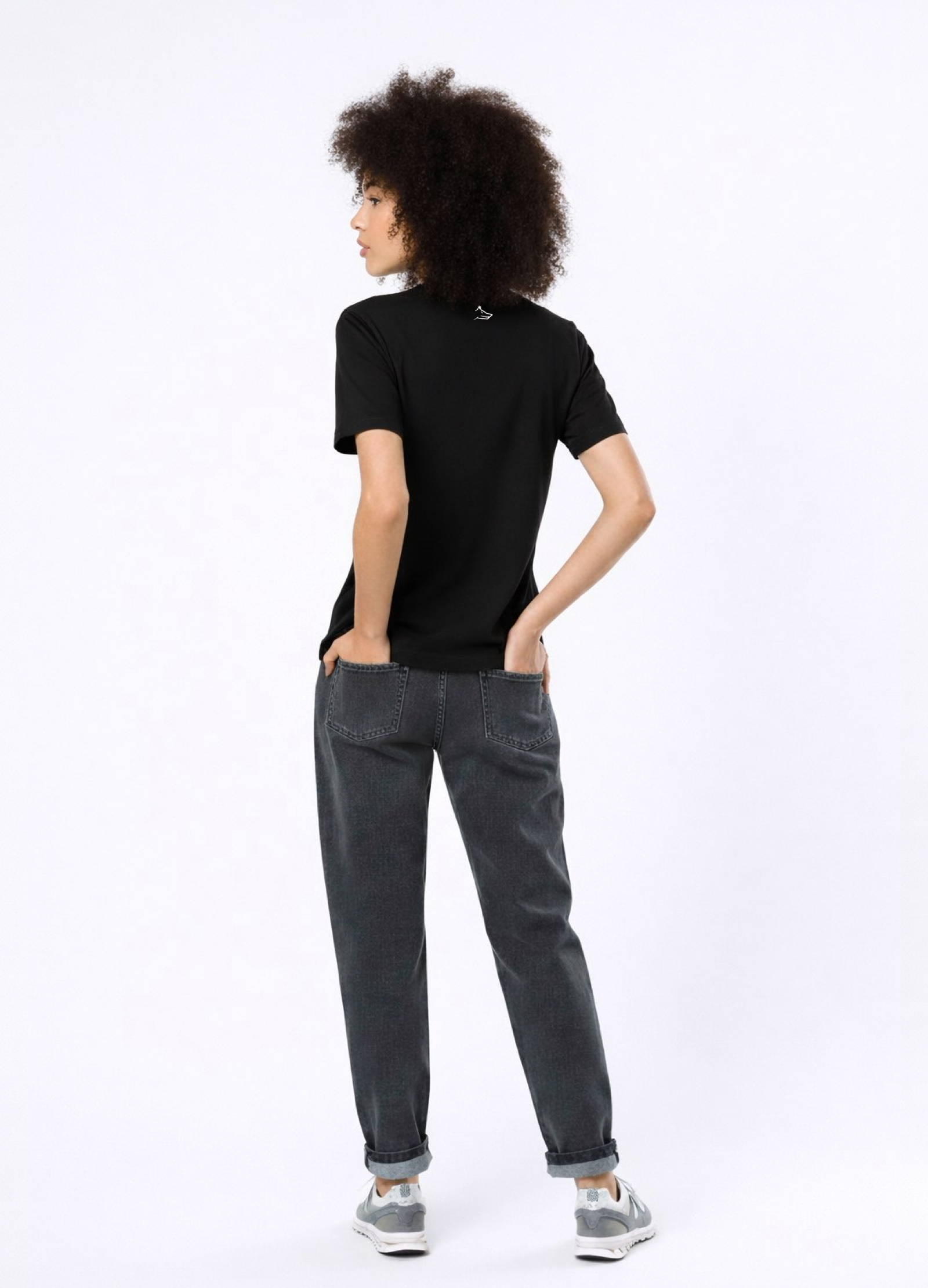 Woman wearing a black Northwind casual t-shirt with minimalist Northwind embroidered logo on the chest and Northwind wolf logo at the back, gray pants and new balance sport shoes