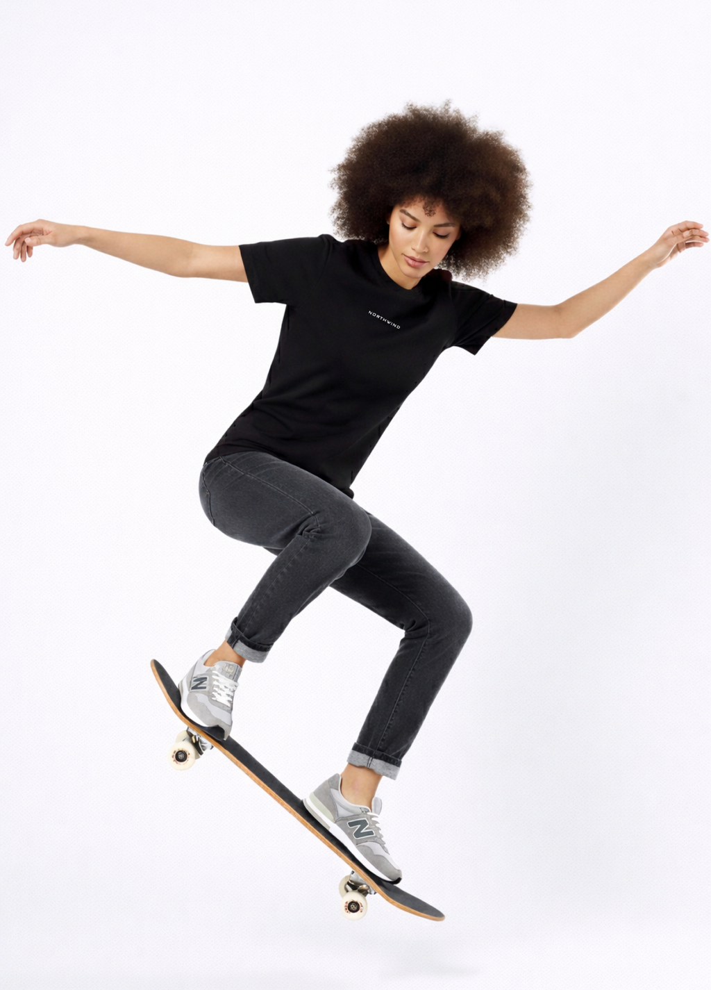 Woman wearing a black Northwind casual t-shirt with minimalist Northwind embroidered logo on the chest and Northwind wolf logo at the back, skateboarding on a white background