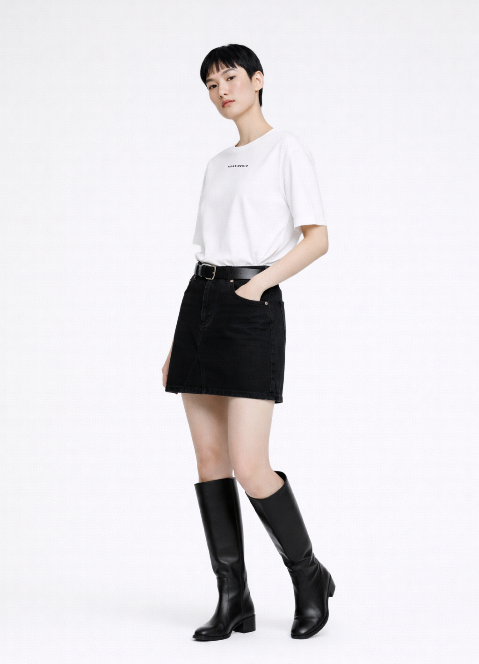 Woman wearing a white Northwind casual t-shirt with minimalist Northwind embroidered wolf logo at the back, black skirt, and black knee-high dr martens boots on a white background