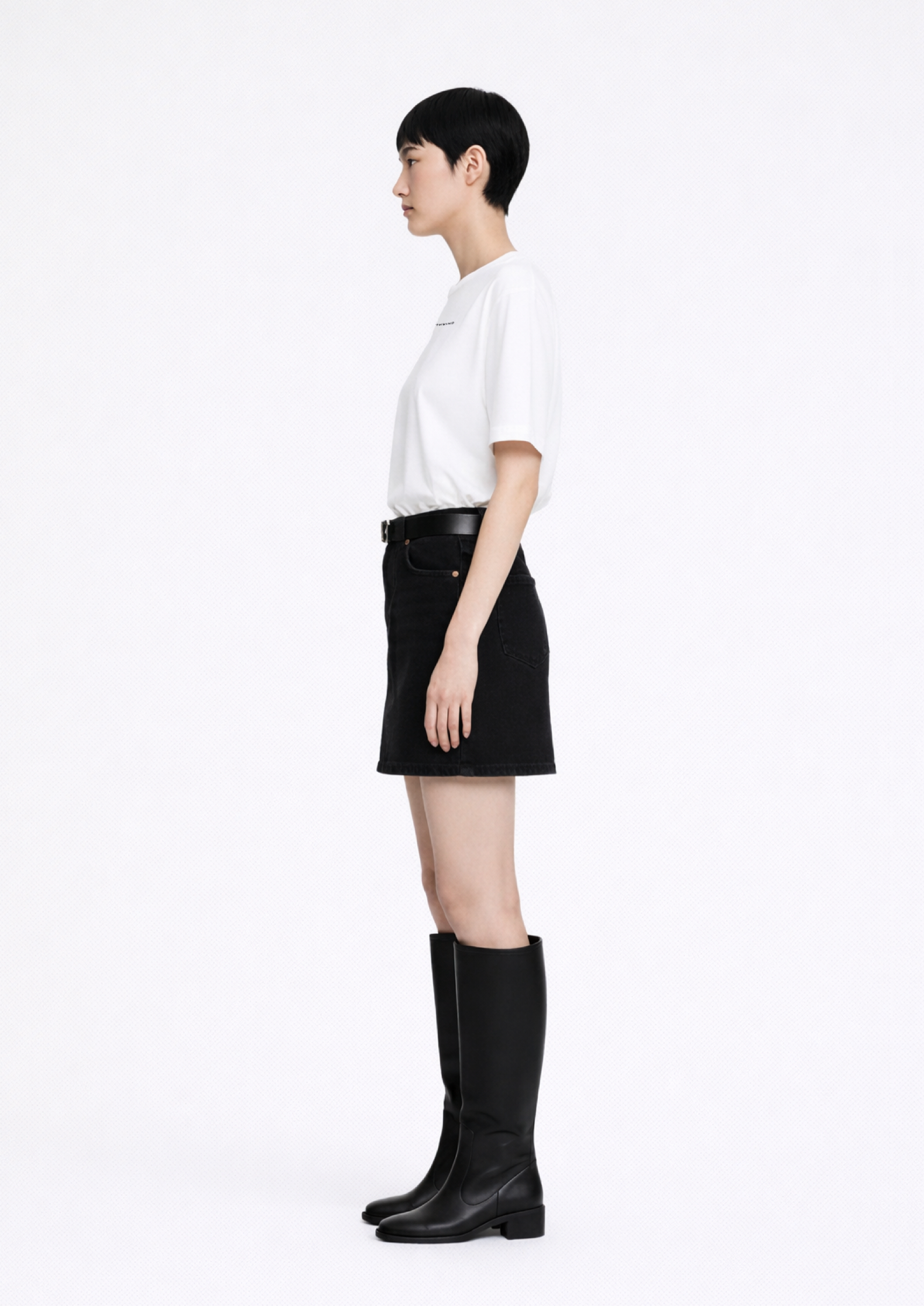 Woman wearing a white Northwind casual t-shirt with minimalist Northwind embroidered wolf logo at the back, black skirt, and black knee-high dr martens boots on a white background