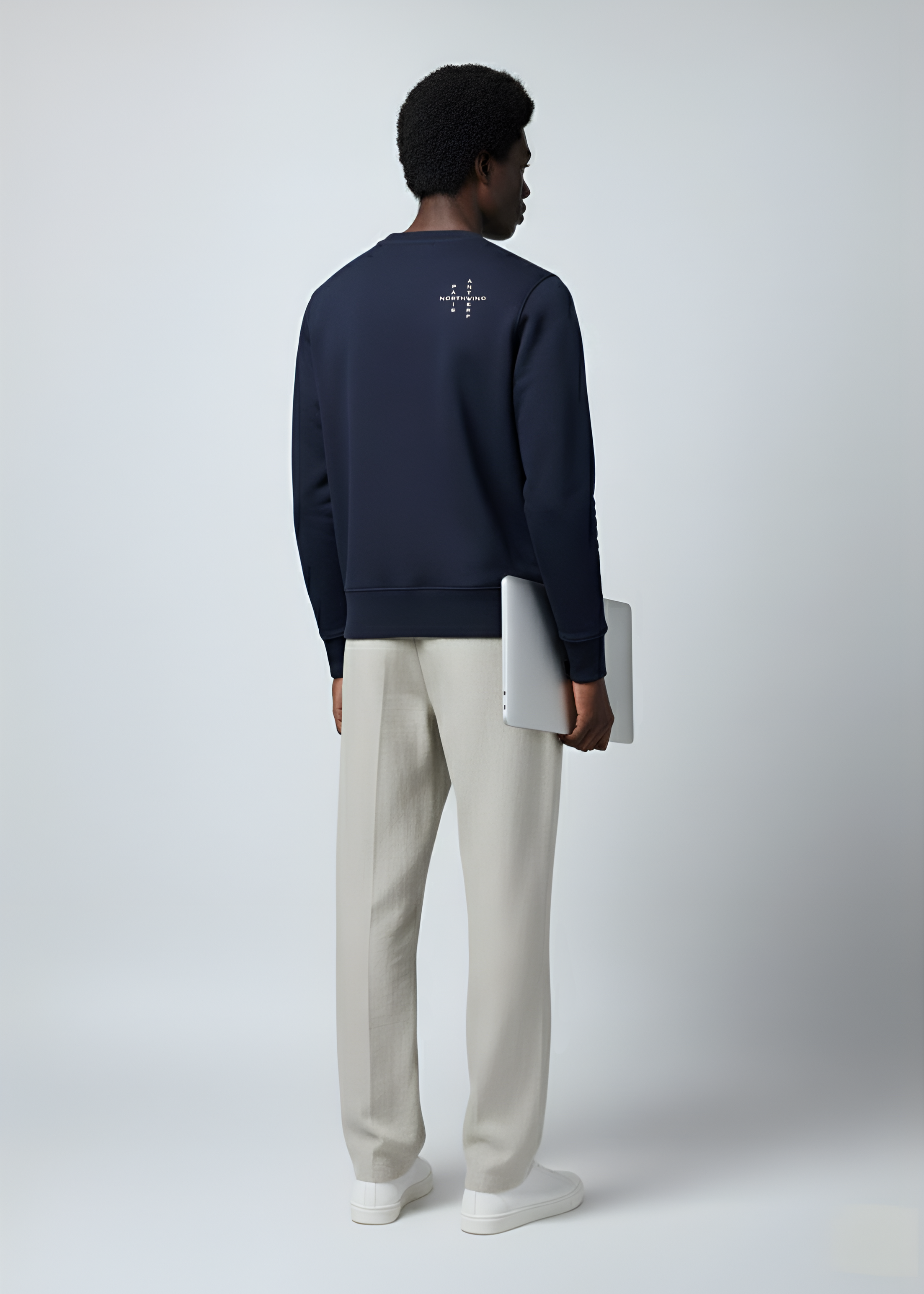 Person wearing a navy Northwind crossword wolf sweater with a white geometric design on the back, holding a white laptop.