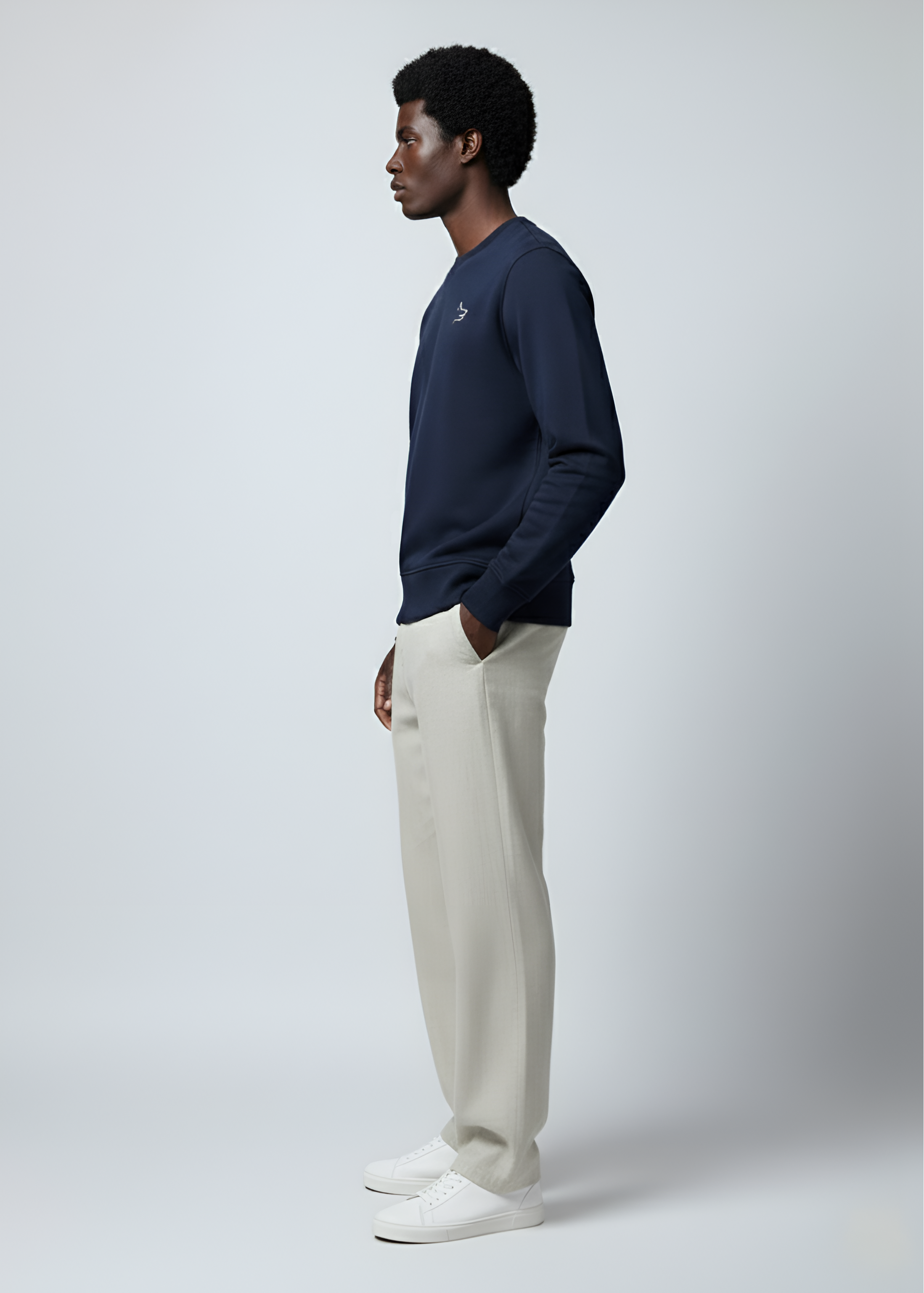 A black man wearing a Northwind crossword Wolf french navy sweatshirt and white pants on a light gray background