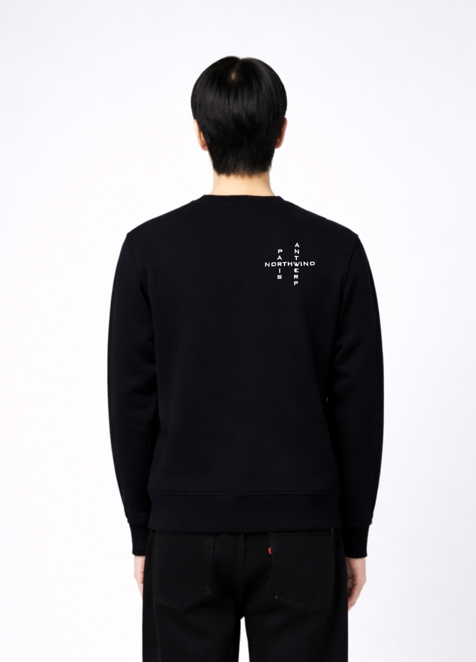 Person wearing a black Northwind sweatshirt with white crossword Paris Antwerp embroidered logo on the back, close back pose