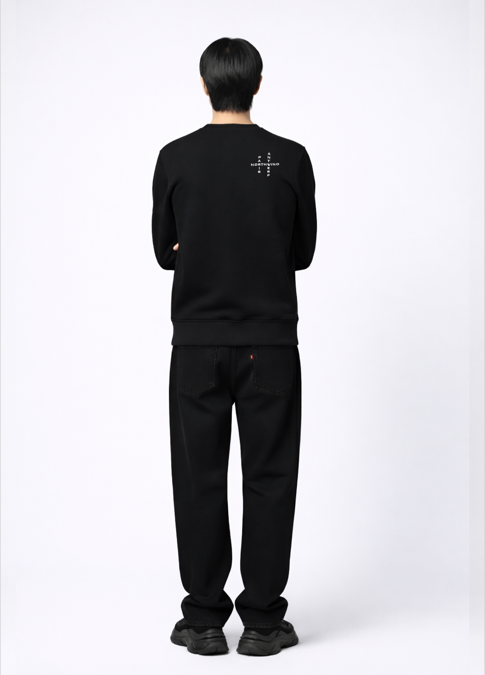 Person wearing a black Northwind sweatshirt with white crossword Paris Antwerp embroidered logo on the back, back pose