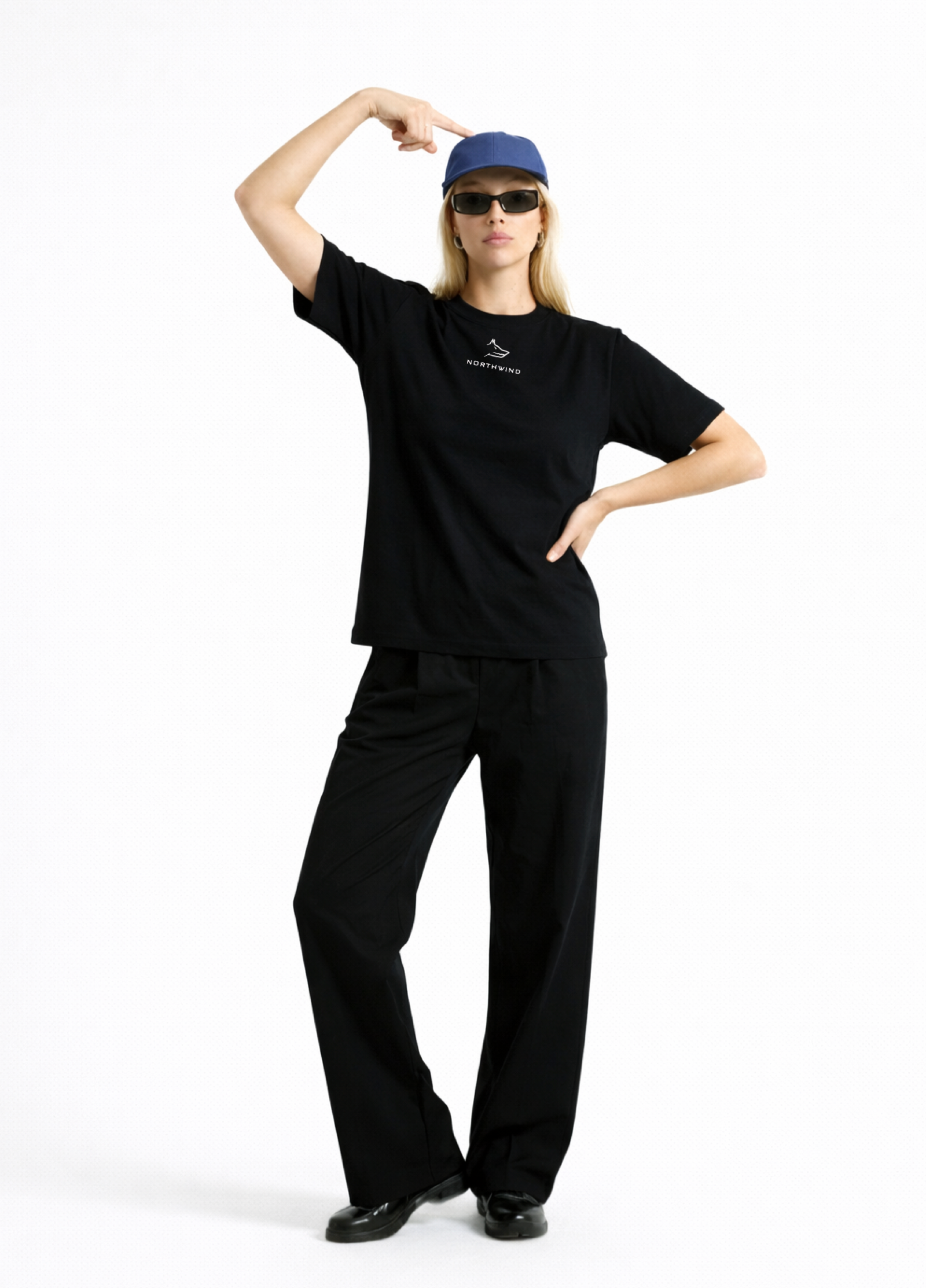 Woman wearing a black Northwind casual t-shirt with minimalist Northwind embroidered wolf logo on the chest, blue hat, black sunglasses and black pants on a white background