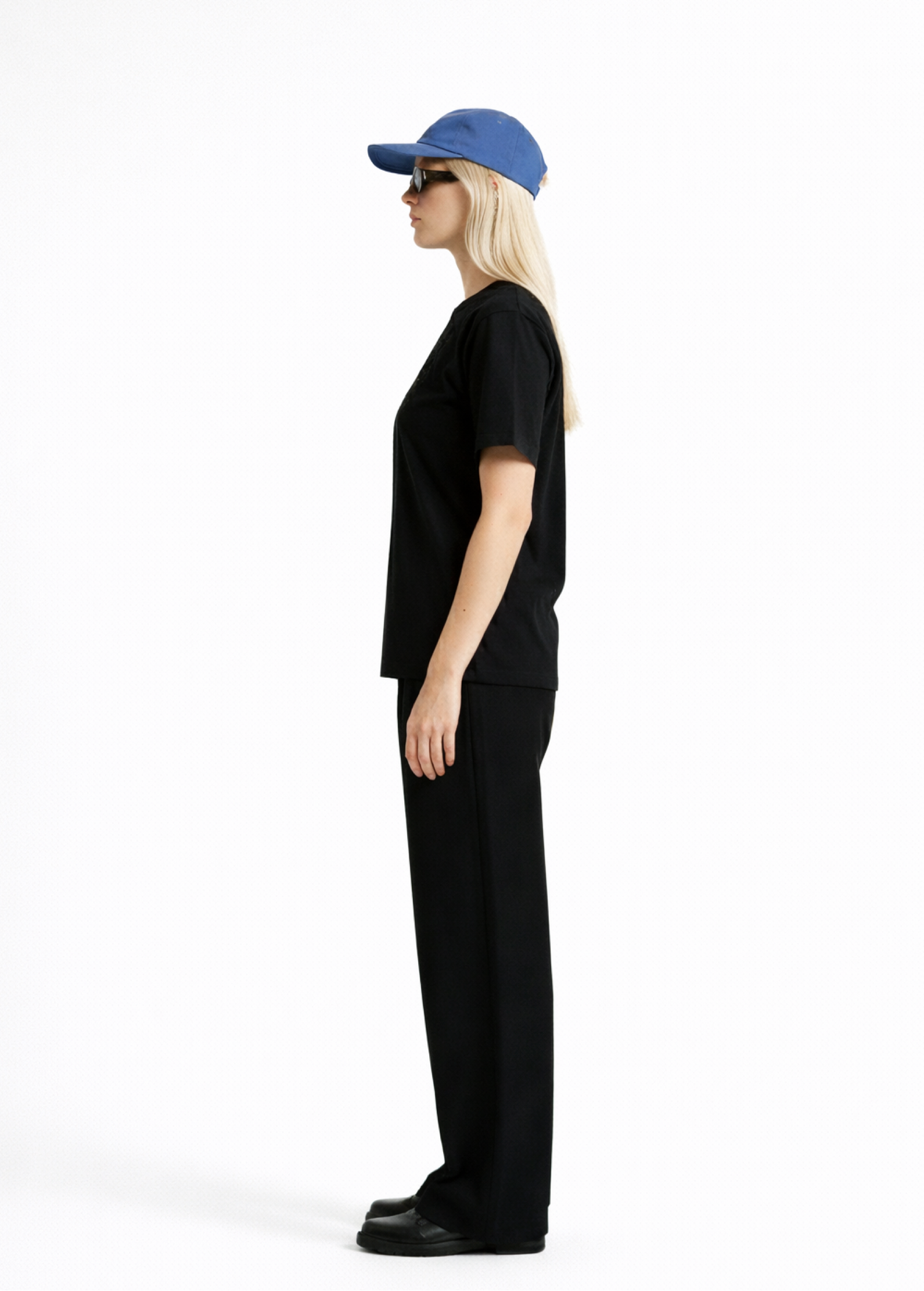 Woman wearing a black Northwind casual t-shirt with minimalist Northwind embroidered wolf logo on the chest, blue hat, black sunglasses and black pants, side pose