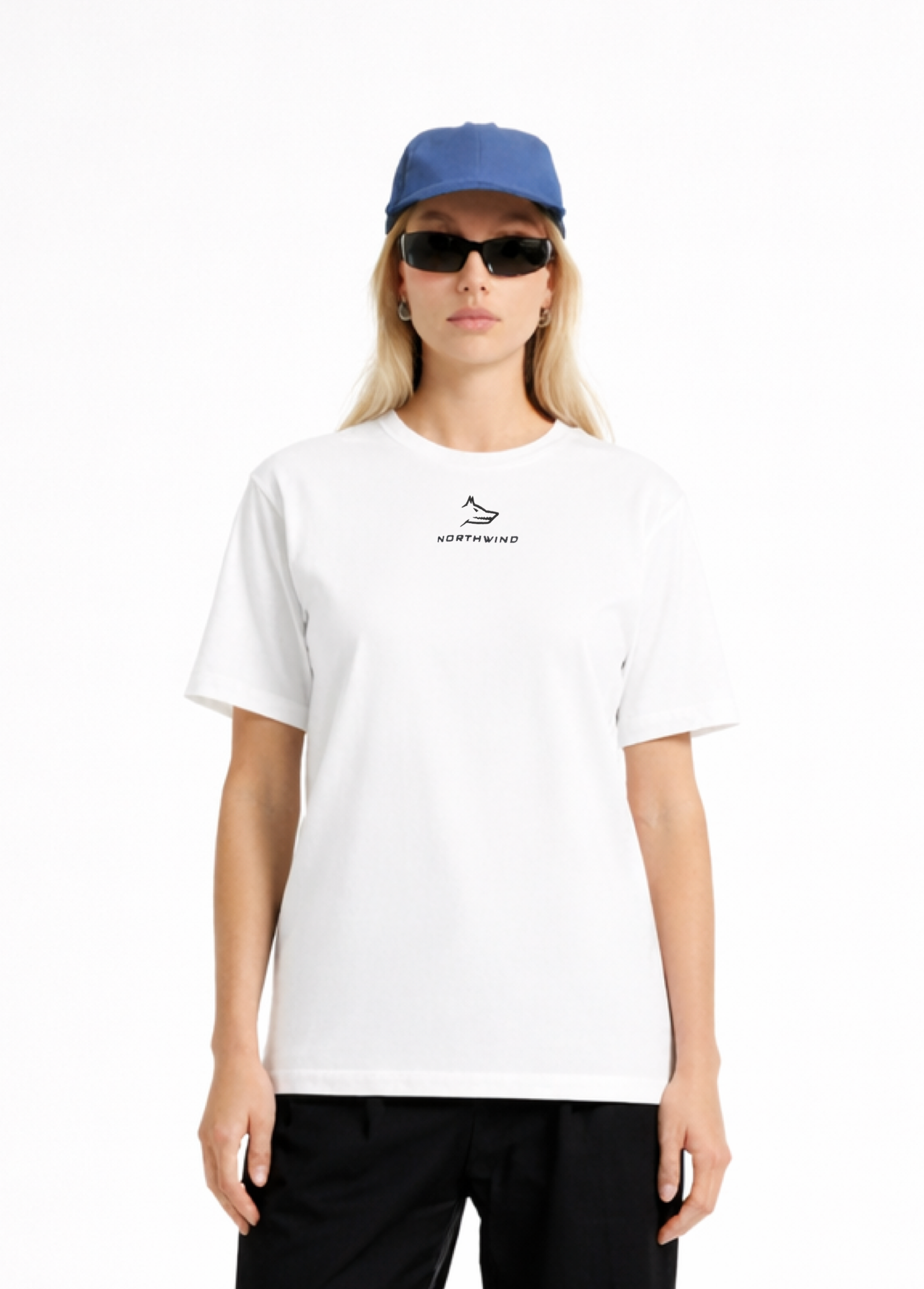 Woman wearing a white Northwind casual t-shirt with minimalist Northwind embroidered wolf logo on the chest, blue hat, black sunglasses and black pants on a white background