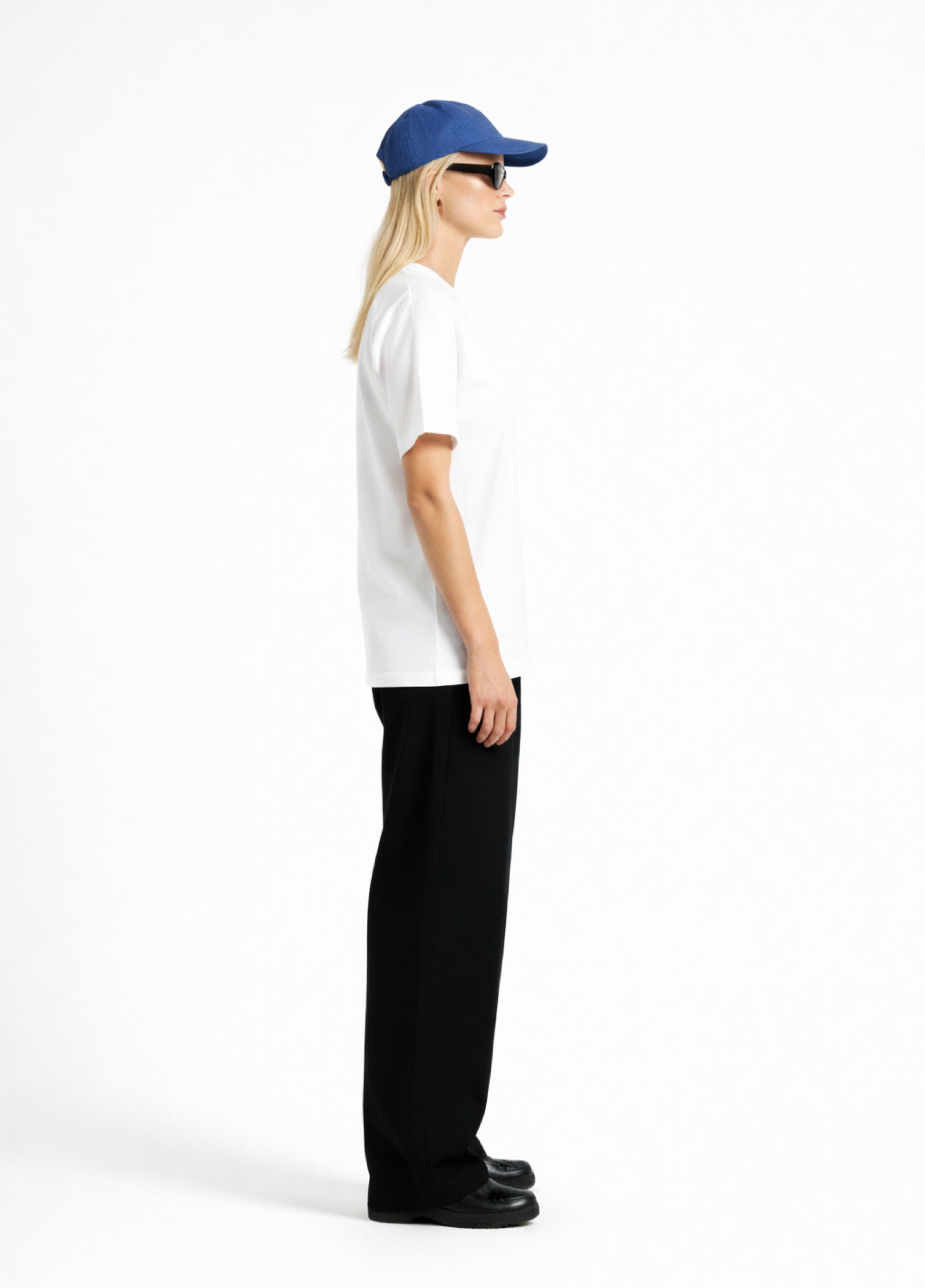 Woman wearing a white Northwind casual t-shirt with minimalist Northwind embroidered wolf logo on the chest, blue hat, black sunglasses and black pants on a white background, having side pose