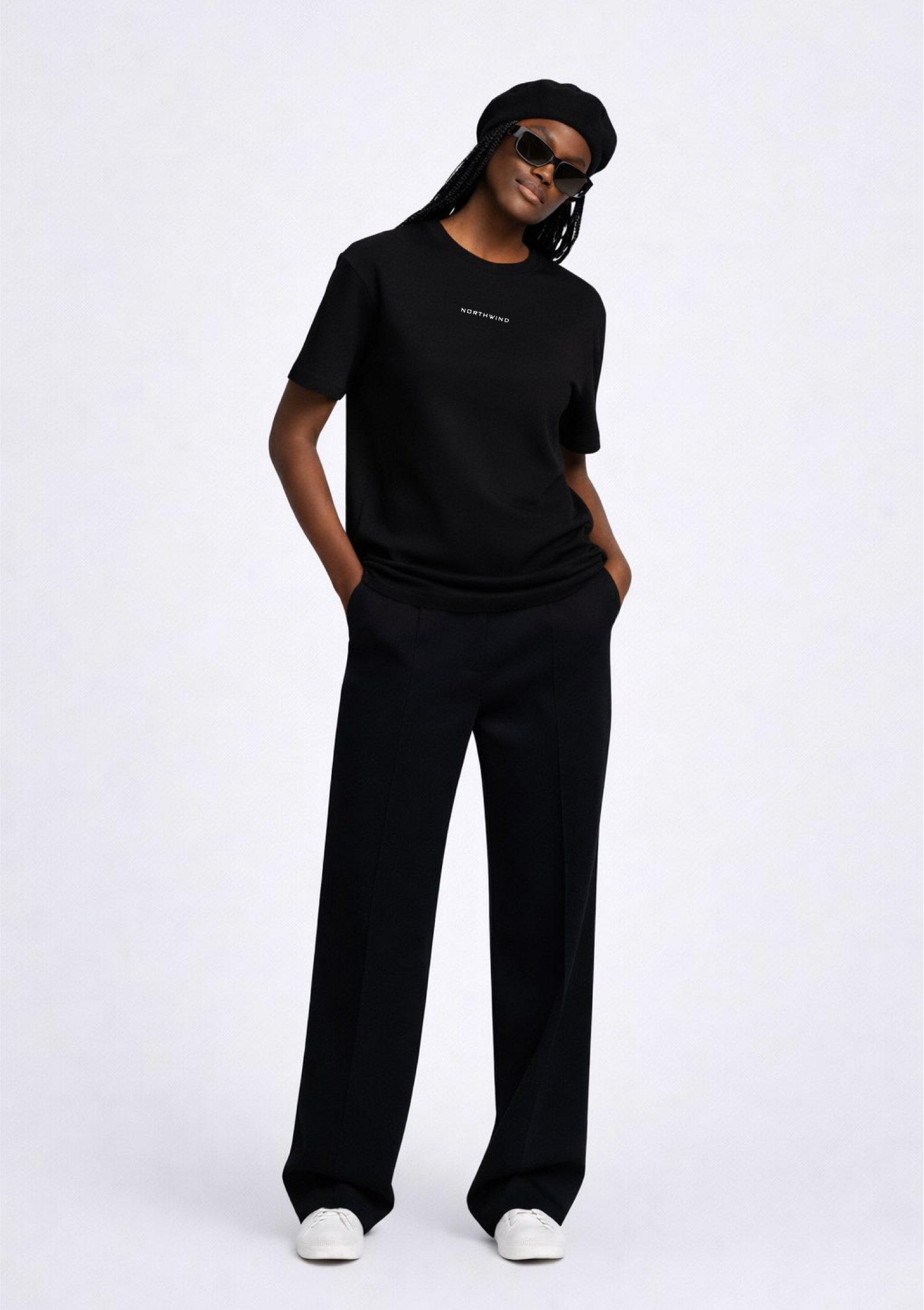 Black woman wearing a black essential Northwind t-shirt with embroidered logo on the chest, Gucci sunglasses, white Adidas Originals and black beret. 