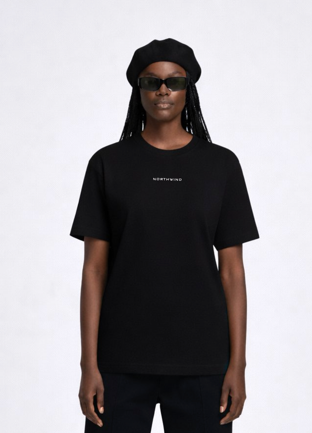 Black woman wearing a black essential Northwind t-shirt with embroidered logo on the chest, Gucci sunglasses and black beret. 
