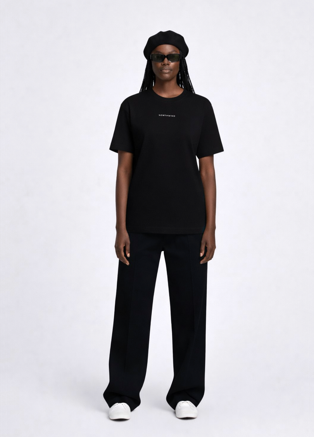 Black woman wearing a black essential Northwind t-shirt with embroidered logo on the chest, Gucci sunglasses, white Adidas Originals and black beret. 