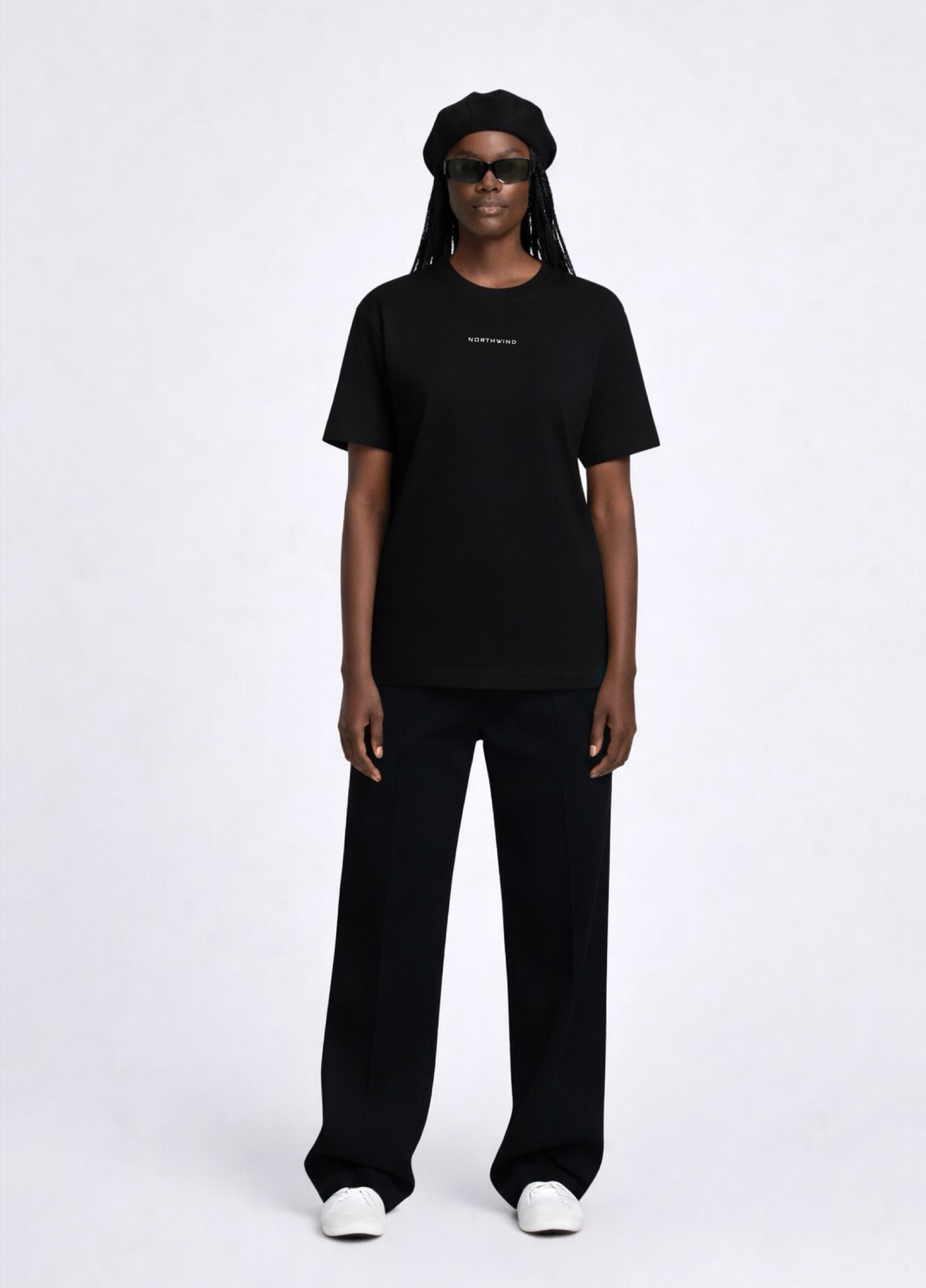 Black woman wearing a black essential Northwind t-shirt with embroidered logo on the chest, Gucci sunglasses, white Adidas Originals and black beret. 