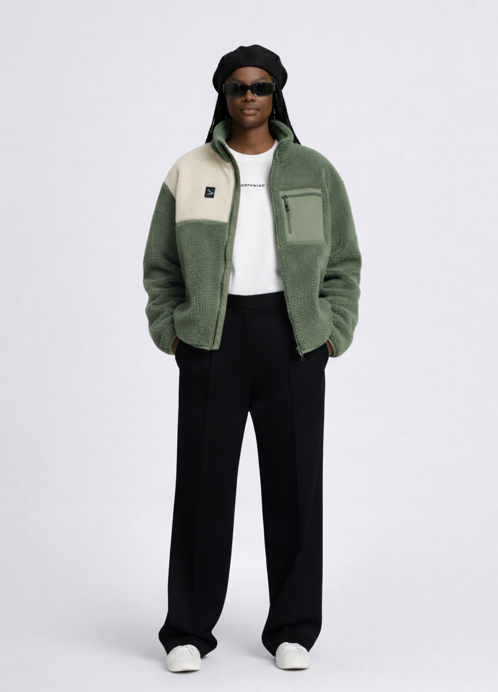 Black woman wearing a white essential Northwind t-shirt with embroidered logo, Gucci sunglasses, Handcrafted Northwind Fleece Jacket with Northwind wolf logo on the chest, black beret and black pants