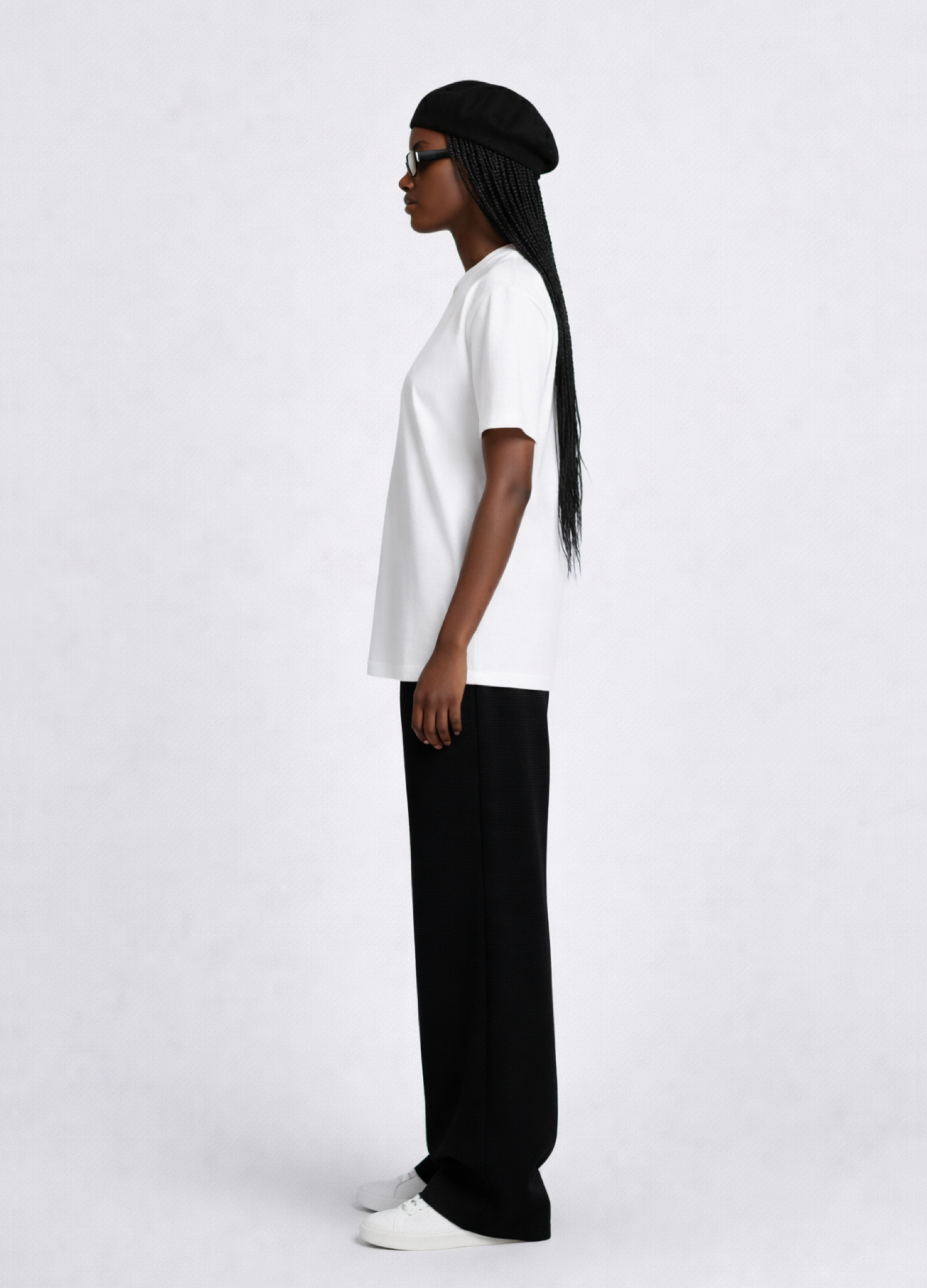 Black woman wearing a white essential Northwind t-shirt with embroidered logo, Gucci sunglasses, black beret and black pants, giving a side pose.