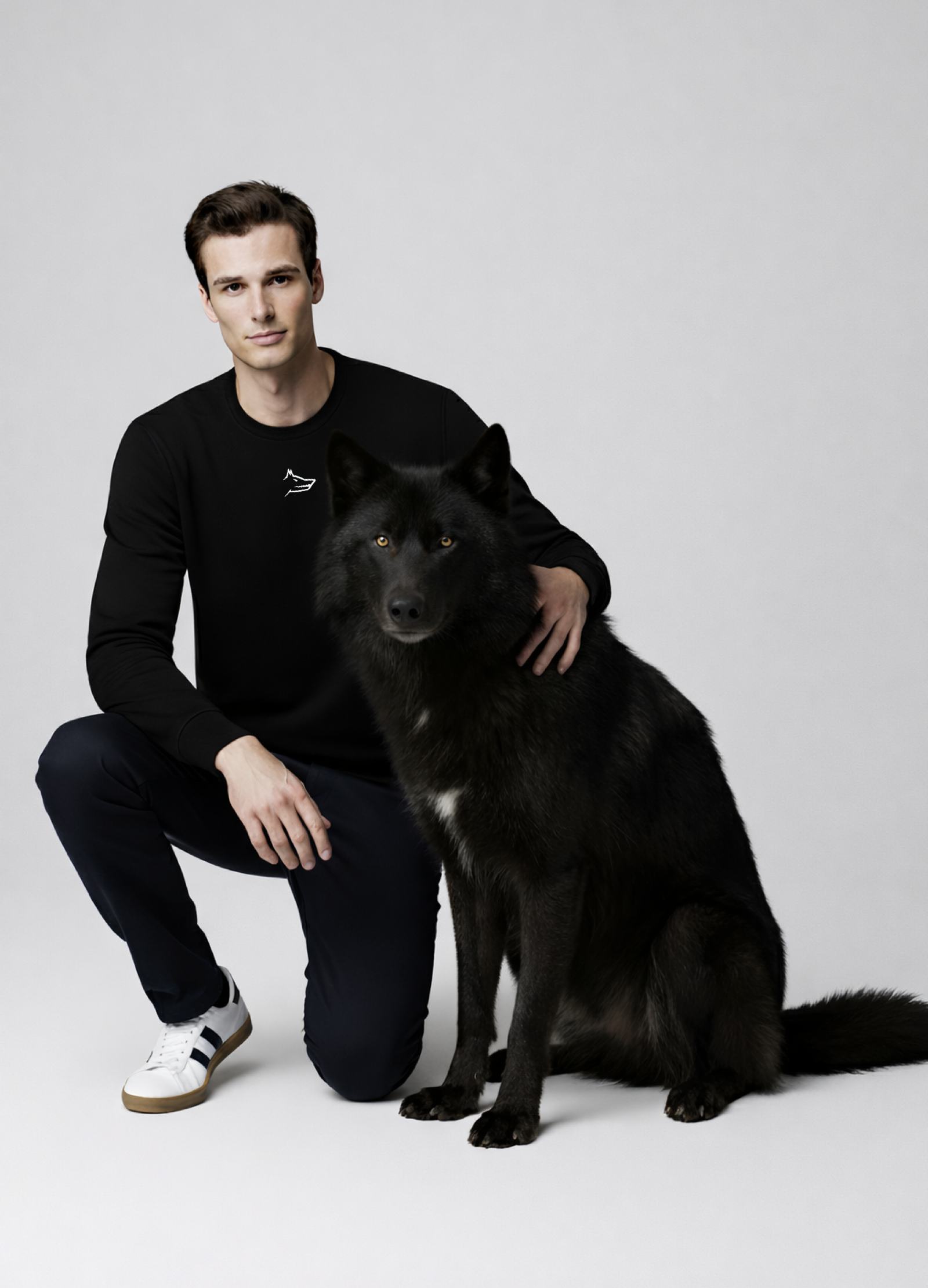 Man wearing a black Northwind sweatshirt with white embroidered Northwind wolf logo on the chest giving a pose with a black wolf