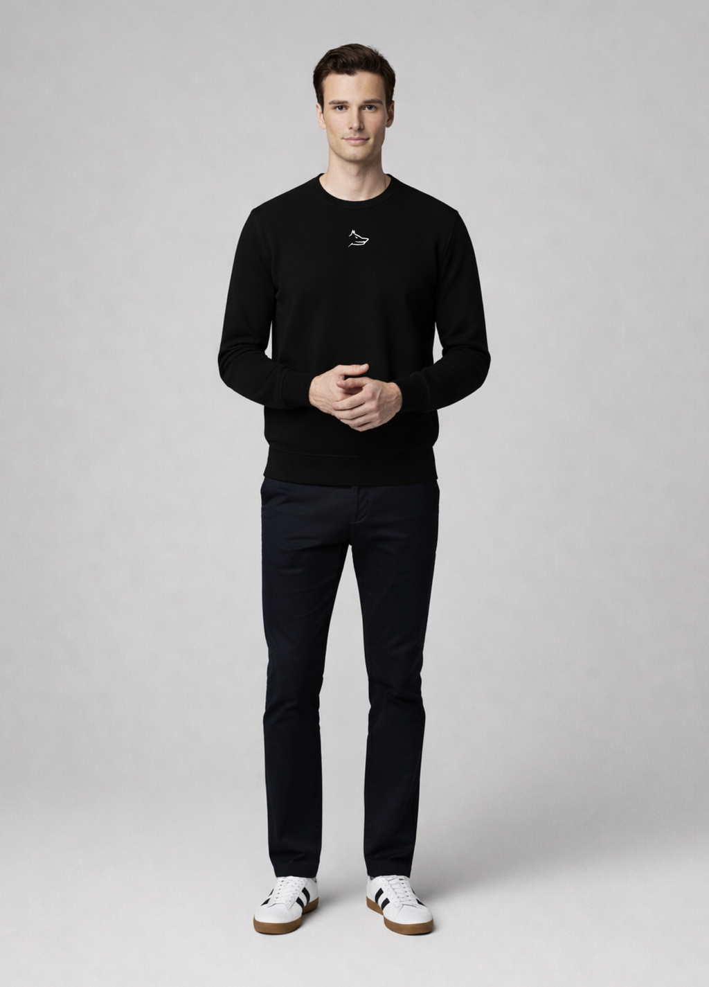 Man wearing a black Northwind sweater with white embroidered Northwind wolf logo on the chest and pants with white sneakers on a light gray background