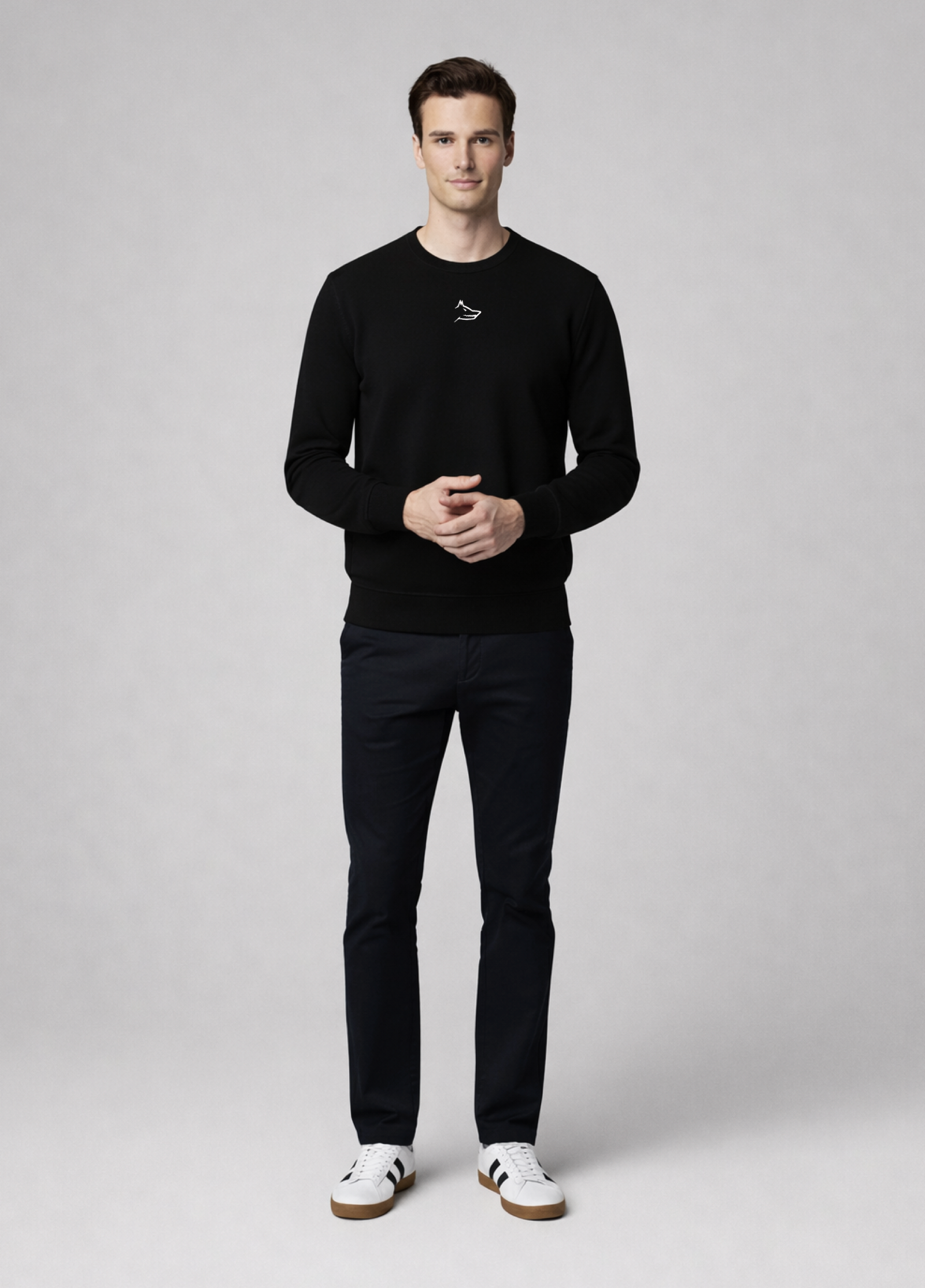 Man wearing a black Northwind sweater with white embroidered Northwind wolf logo on the chest and pants with white sneakers on a light gray background