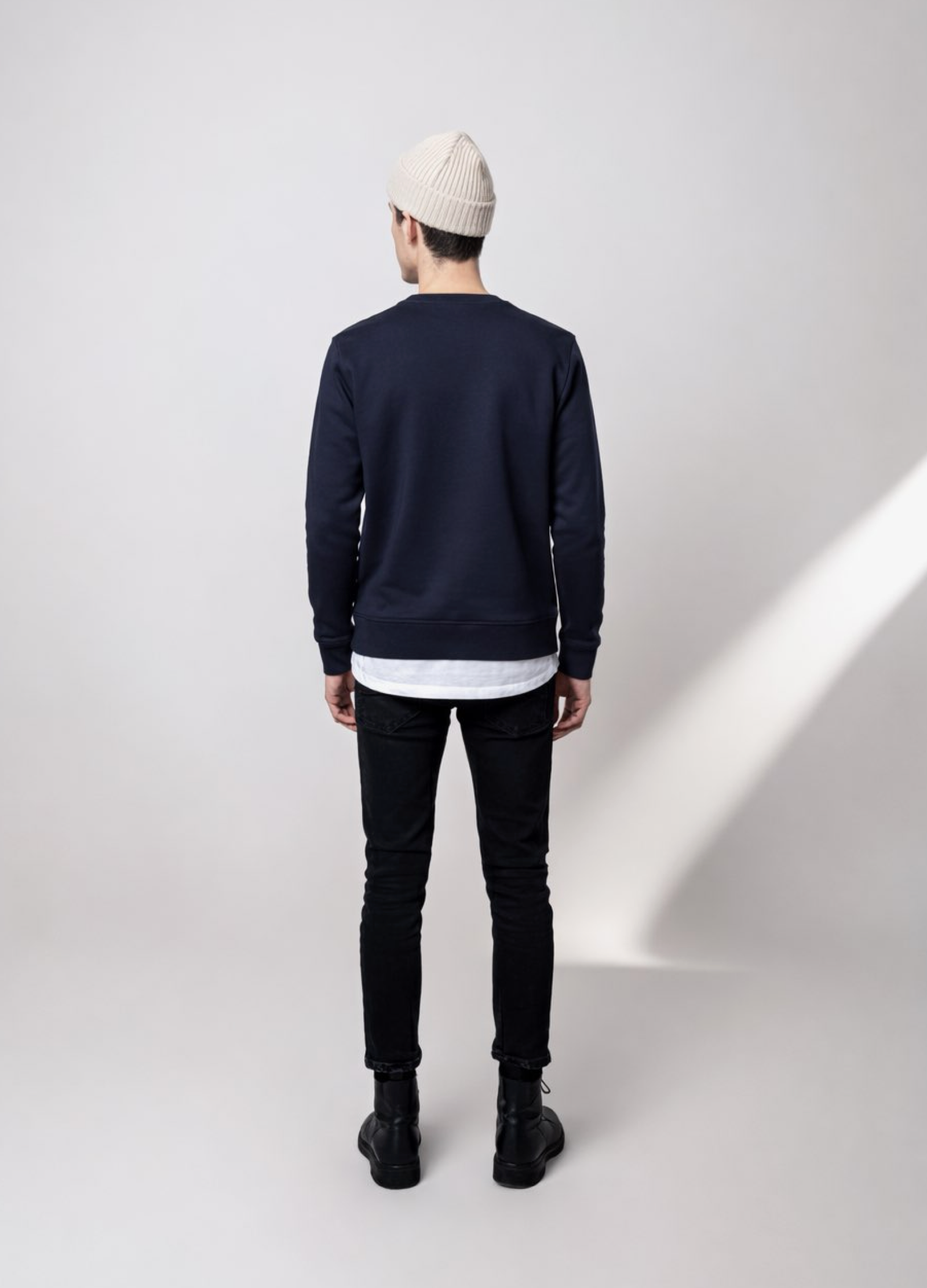 Person wearing a navy blue Northwind lone wolf sweatshirt, black jeans, and a sand cream organic beanie, back pose