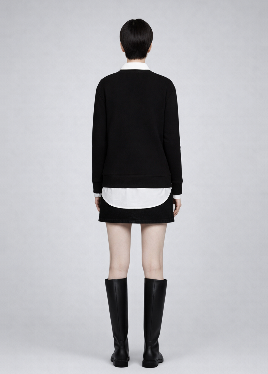 Woman wearing a black Northwind sweatshirt white shirt, black skirt, and black boots on a plain background