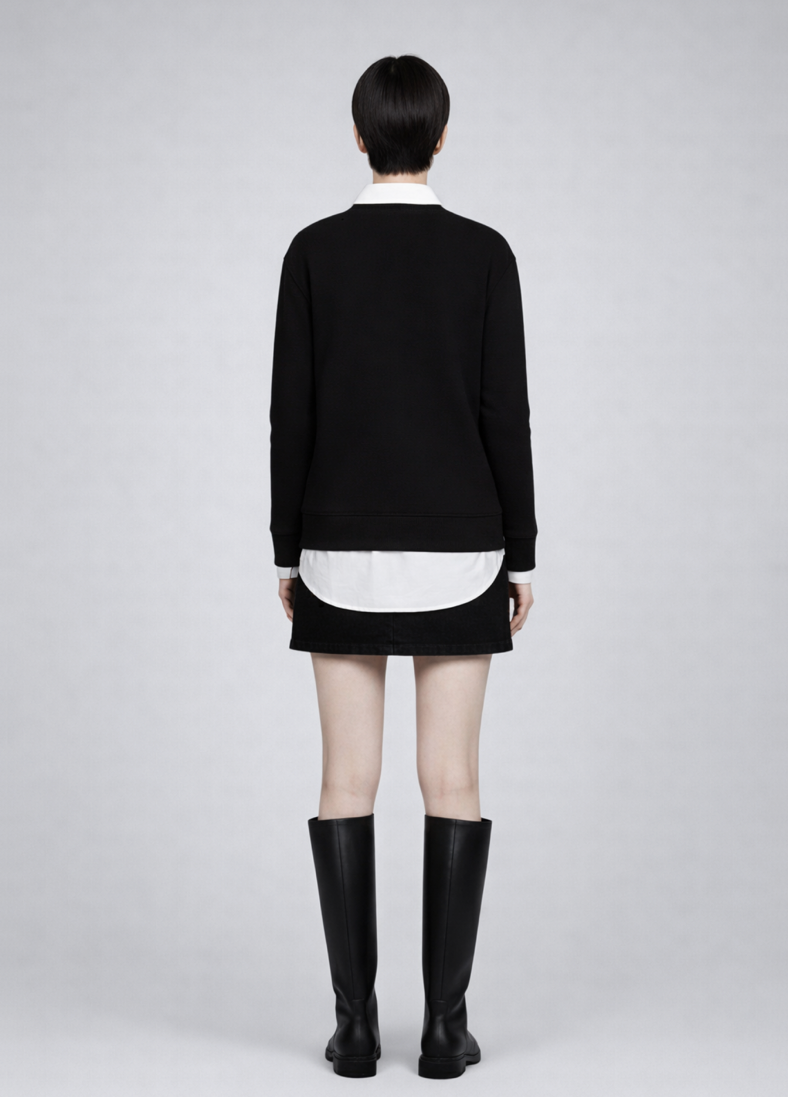 Woman wearing a black Northwind sweatshirt white shirt, black skirt, and black boots on a plain background