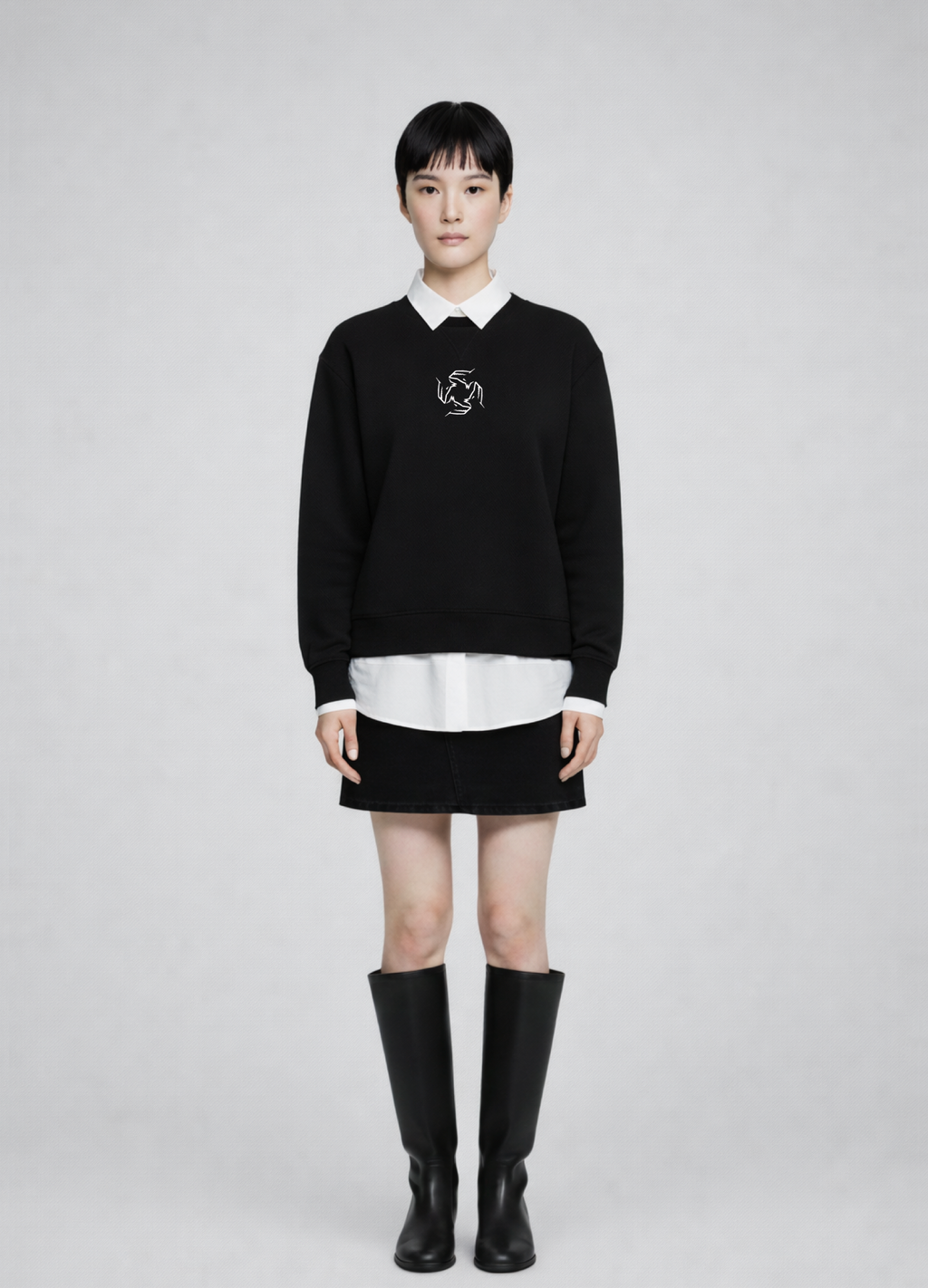 Woman wearing a black Northwind storm of wolves sweatshirt with a white collar, white shirt, black skirt, and black knee-high boots on a gray background