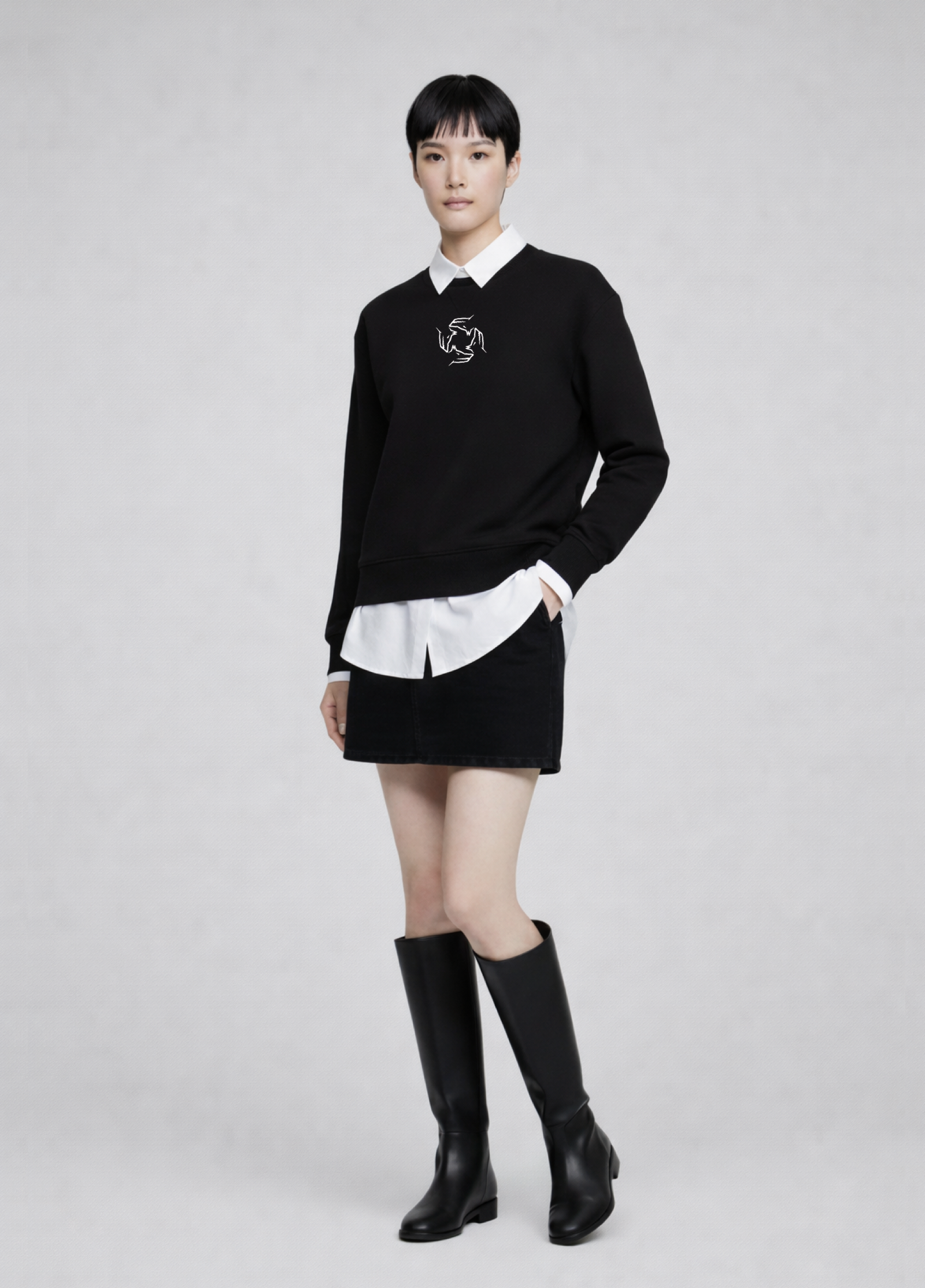 Woman wearing a black Northwind storm of wolves sweatshirt with a white collar, white shirt, black skirt, and black knee-high boots on a light gray background.