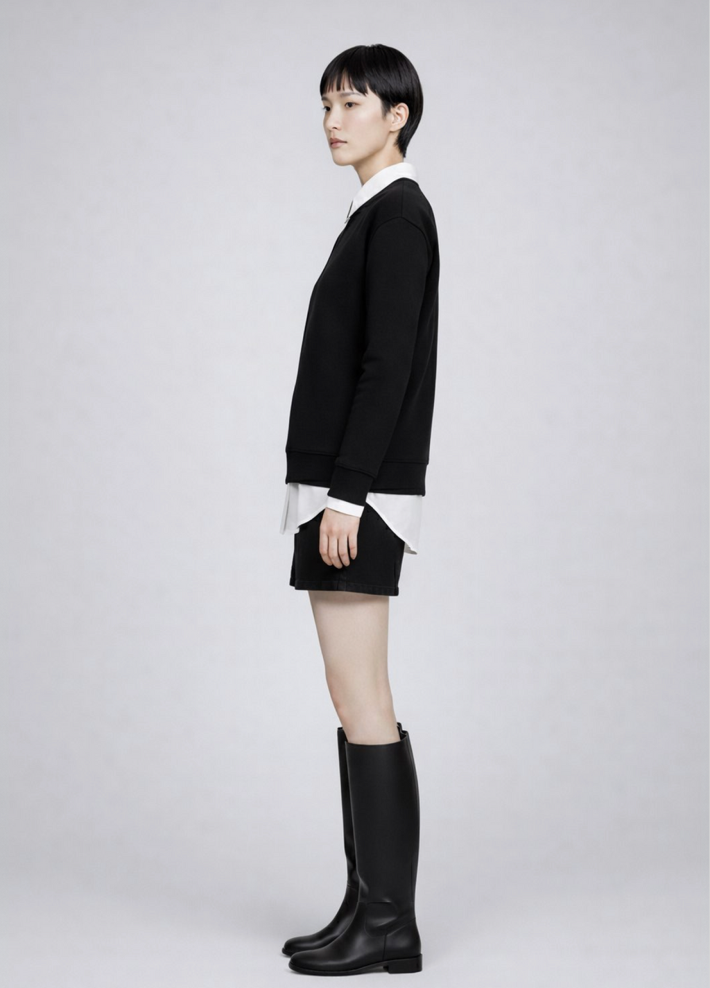 woman wearing a black Northwind Storm of Wolves sweatshirt with embroidered logo, white shirt, black skirt, and black knee-high boots on a light gray background