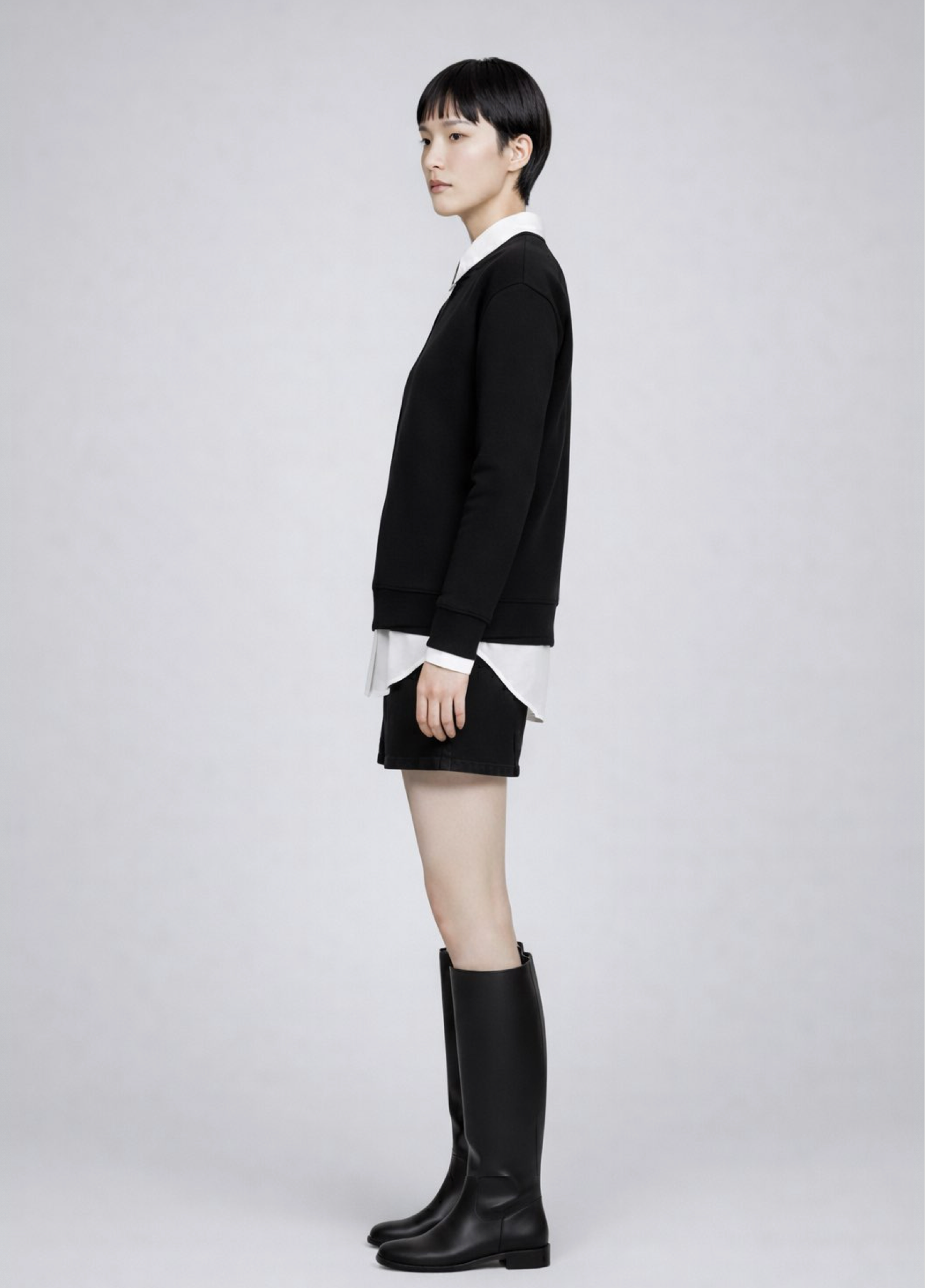 woman wearing a black Northwind Storm of Wolves sweatshirt with embroidered logo, white shirt, black skirt, and black knee-high boots on a light gray background