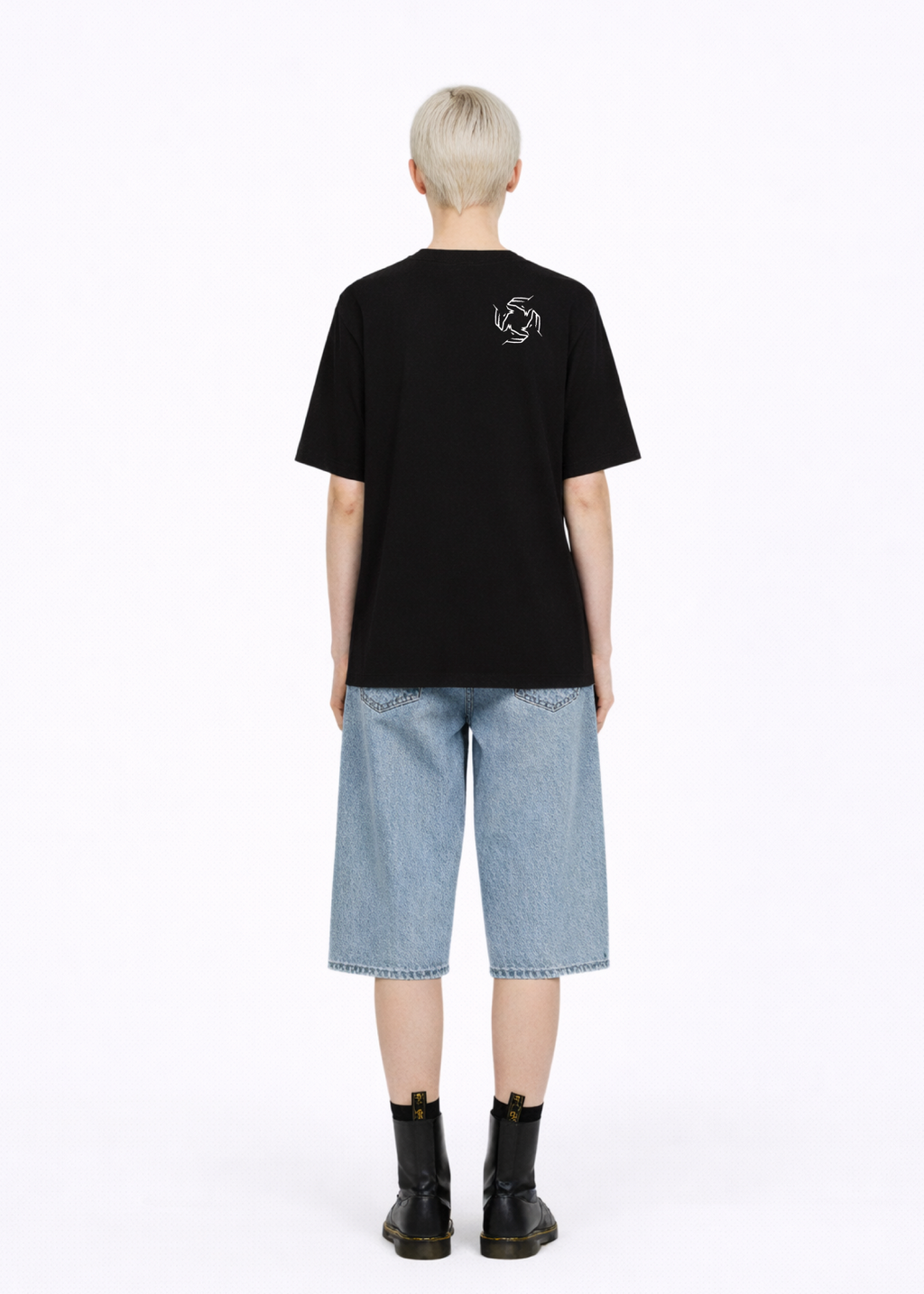Blond, short hair girl wearing a black Northwind casual storm of wolves t-shirt with Northwind storm of wolves logo embroidered on the back, blue denim Carhartt oversized shorts, black belt, and black Dr. Martens boots