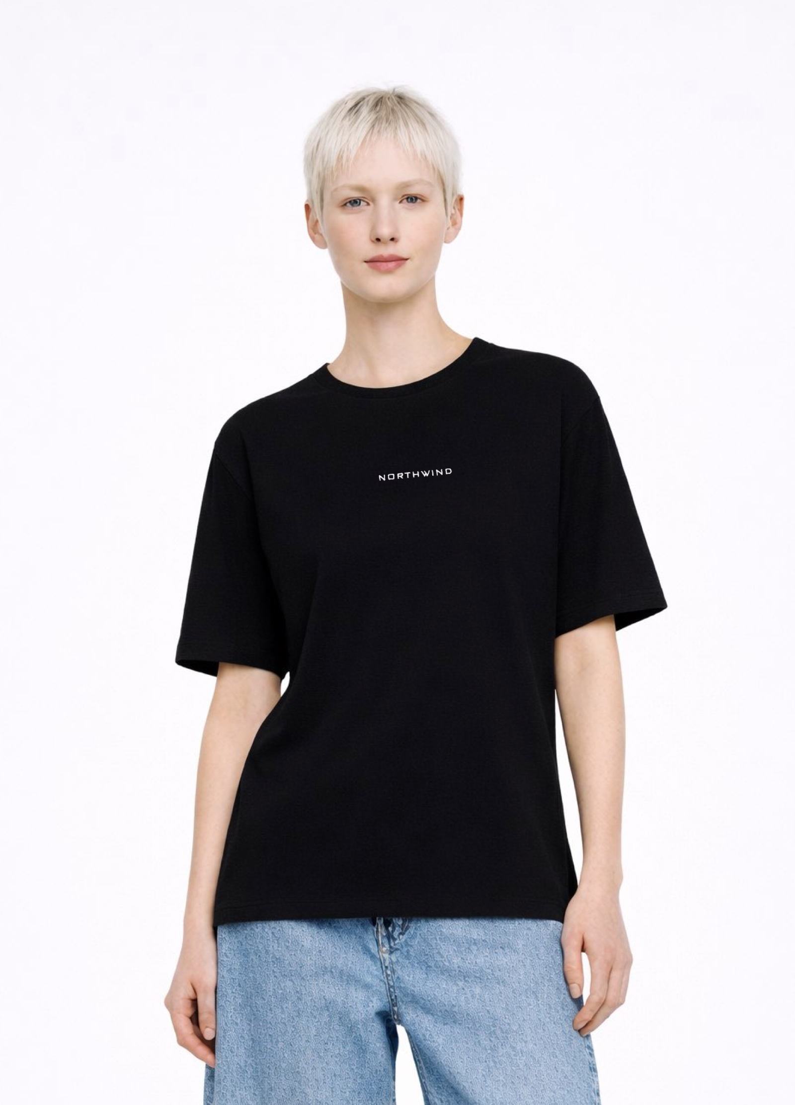 Blond, short hair girl wearing a black Northwind casual storm of wolves t-shirt with Northwind logo embroidered on the chest, blue denim Carhartt oversized shorts, black belt, and black Dr. Martens boots on a white background