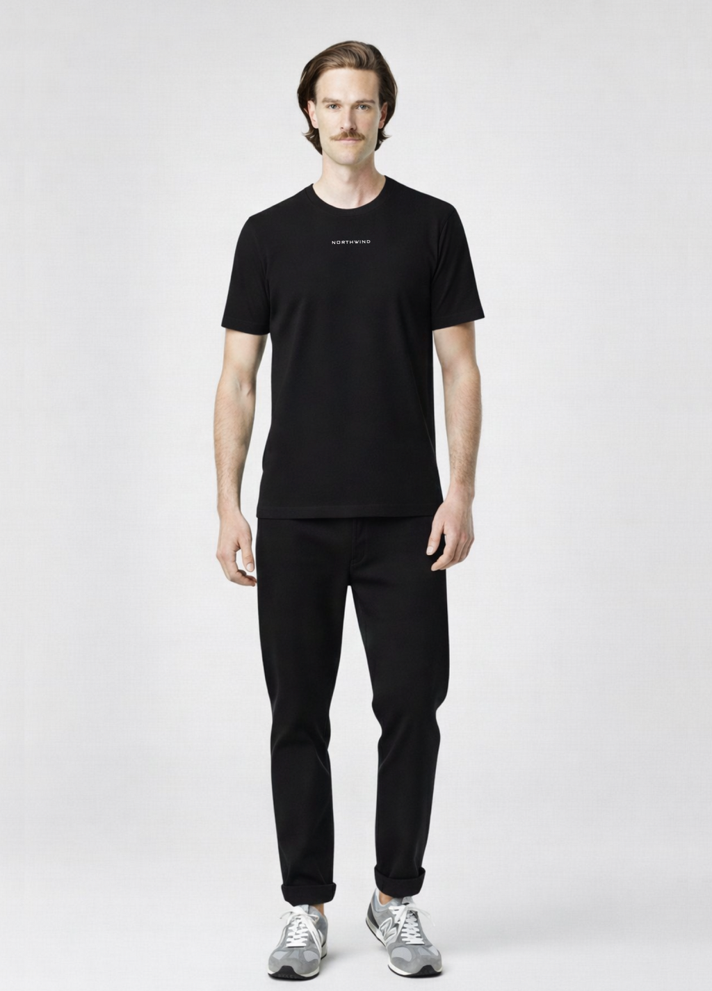 Man wearing a black Northwind storm of wolves t-shirt with embroidered Northwind logo on the chest, gray new Balance shoes