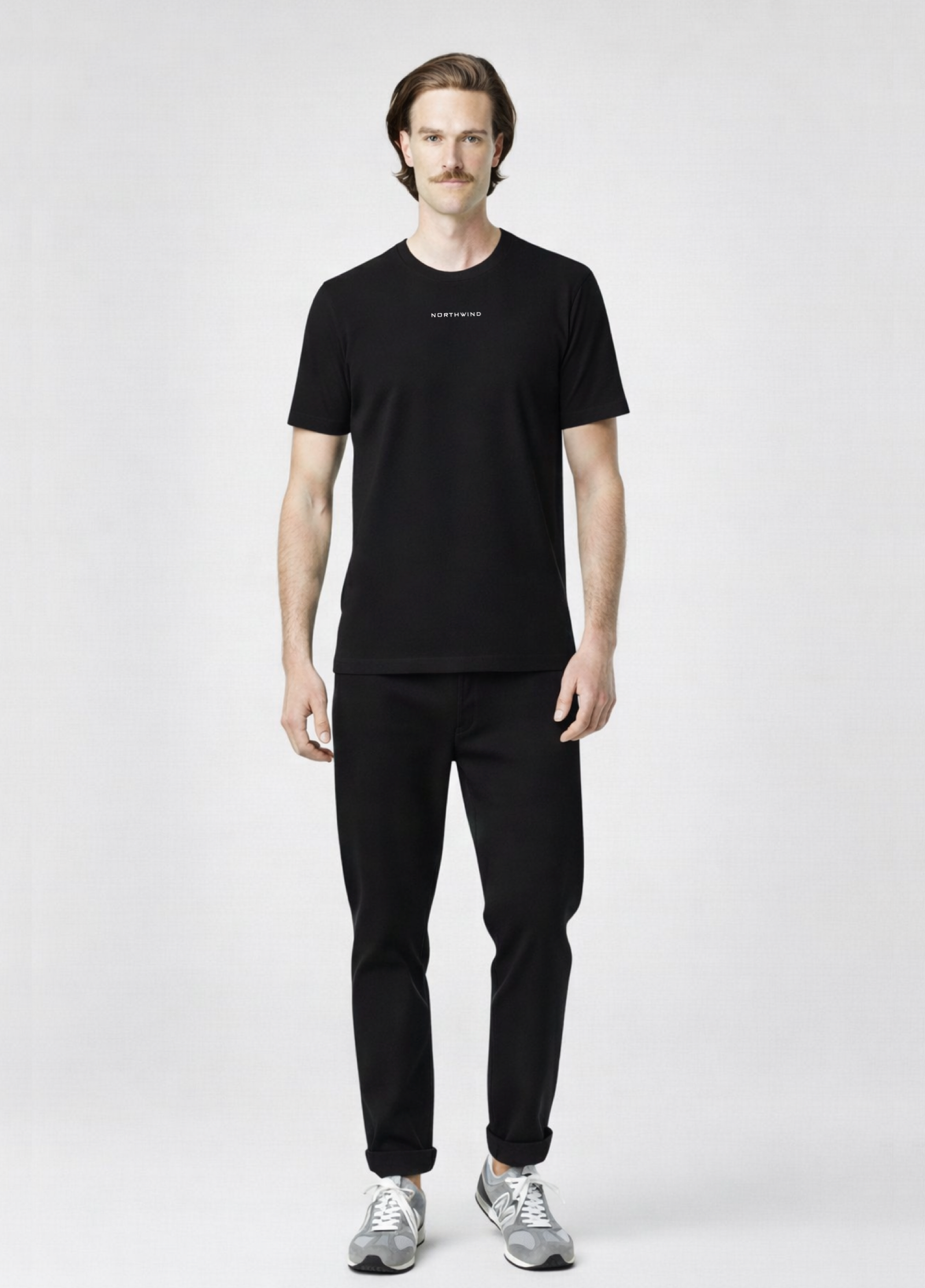 Man wearing a black Northwind storm of wolves t-shirt with embroidered Northwind logo on the chest, gray new Balance shoes