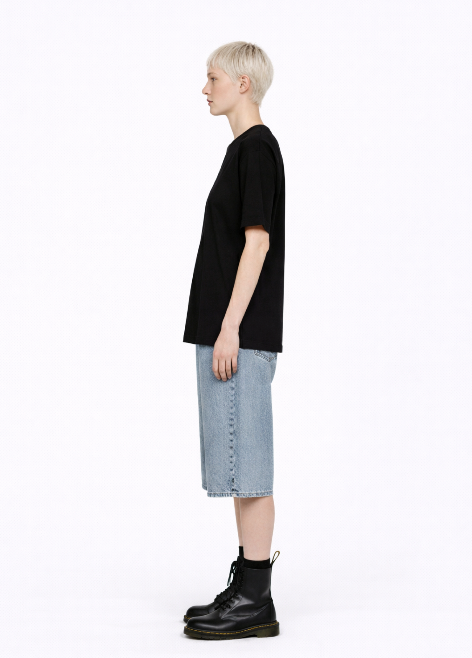 Blond, short hair girl wearing a black Northwind casual storm of wolves t-shirt with Northwind logo embroidered on the chest, blue denim Carhartt oversized shorts, and black Dr. Martens boots