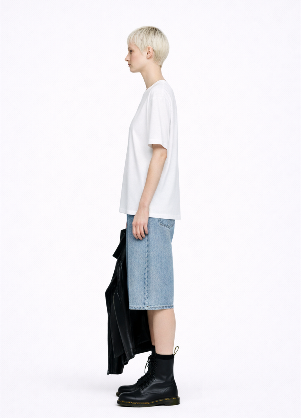 Blond, short hair girl wearing a white Northwind casual storm of wolves t-shirt with Northwind logo embroidered on the chest, blue denim Carhartt oversized shorts, black belt, and black Dr. Martens boots on a white background
